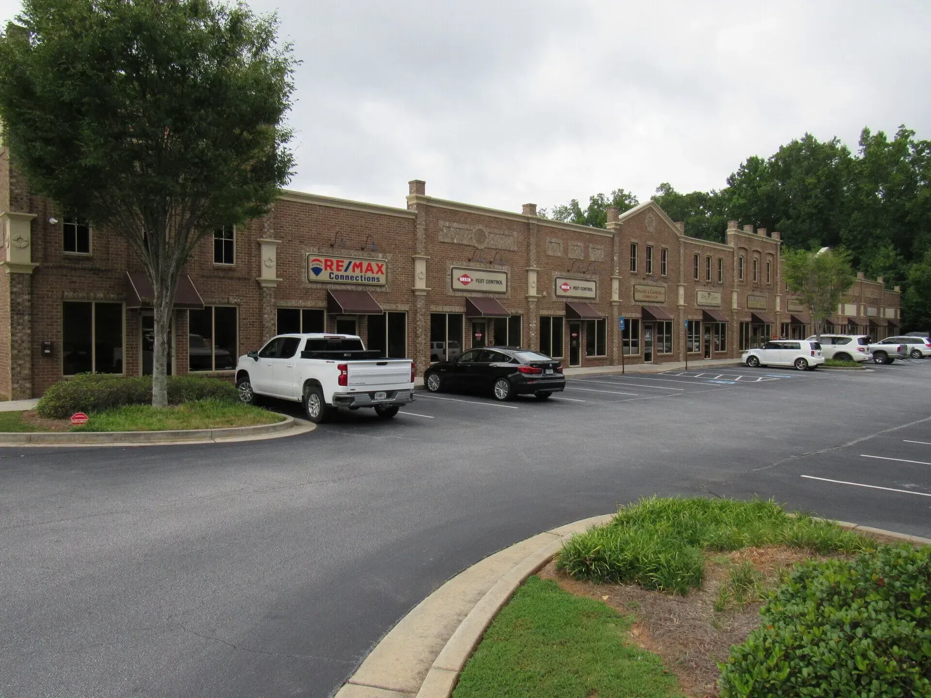 Brick commercial buildings with storefronts and a parking lot; cloudy sky.