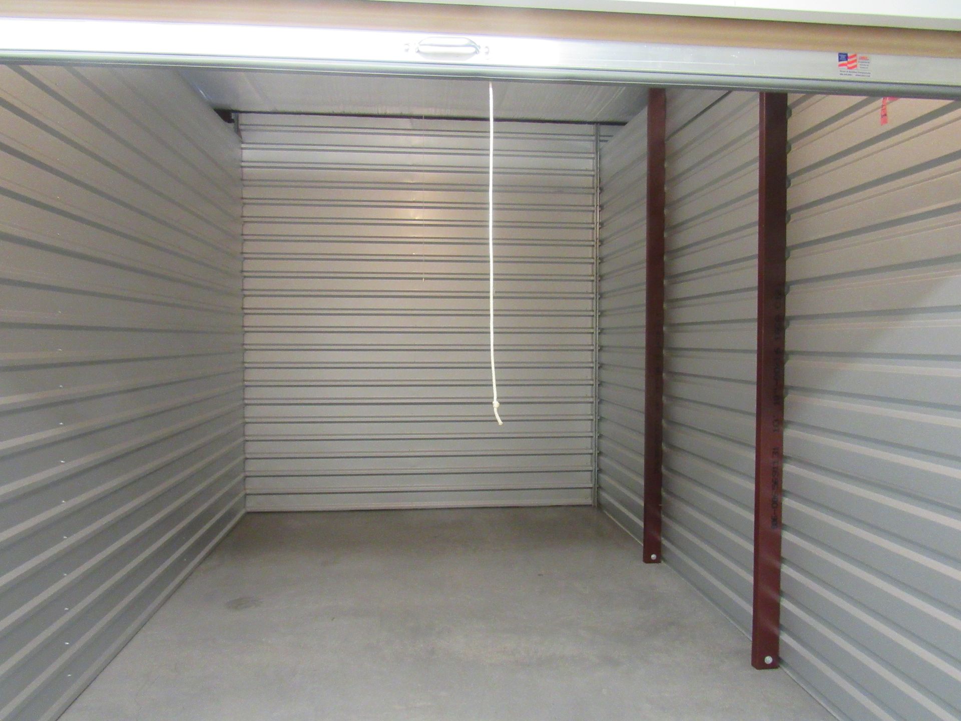 Empty, silver-walled storage unit with a roll-up door, metal beams on the right.