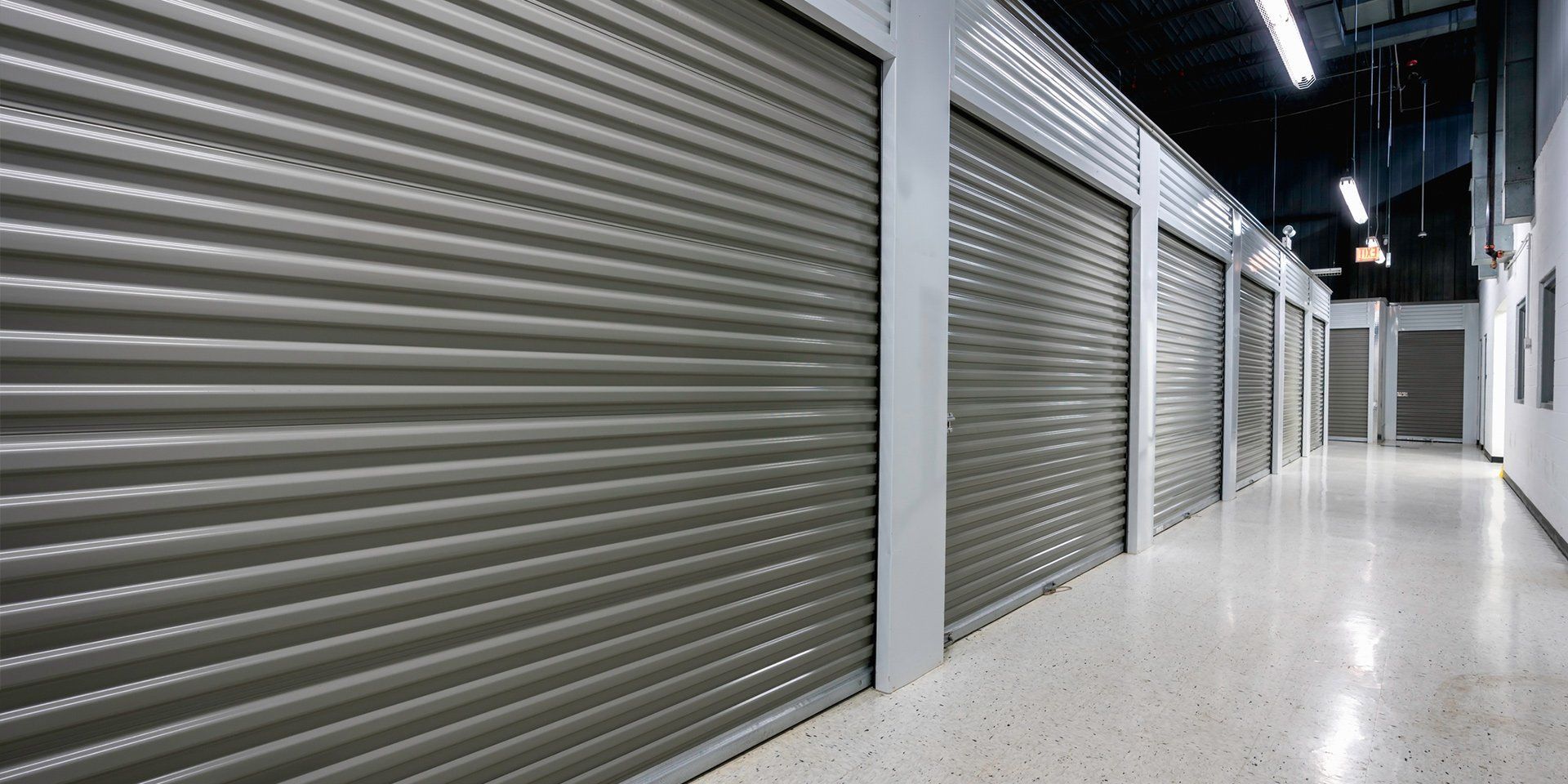 Brick commercial building with shops, cars parked in front, overcast sky.