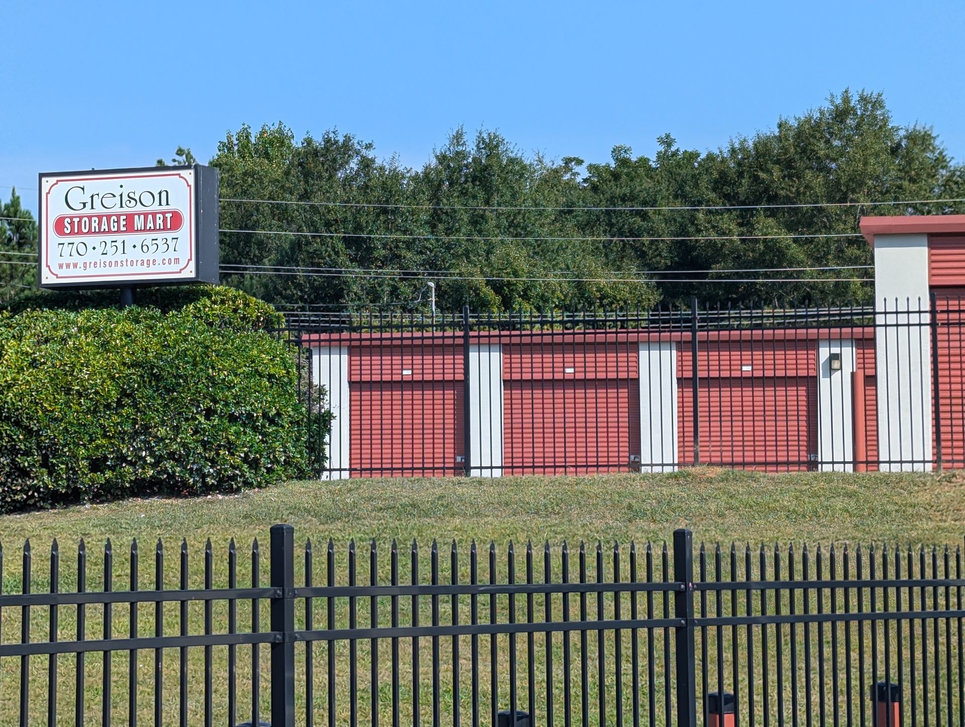 Sign for Clarion Storage with red storage units behind a black fence.
