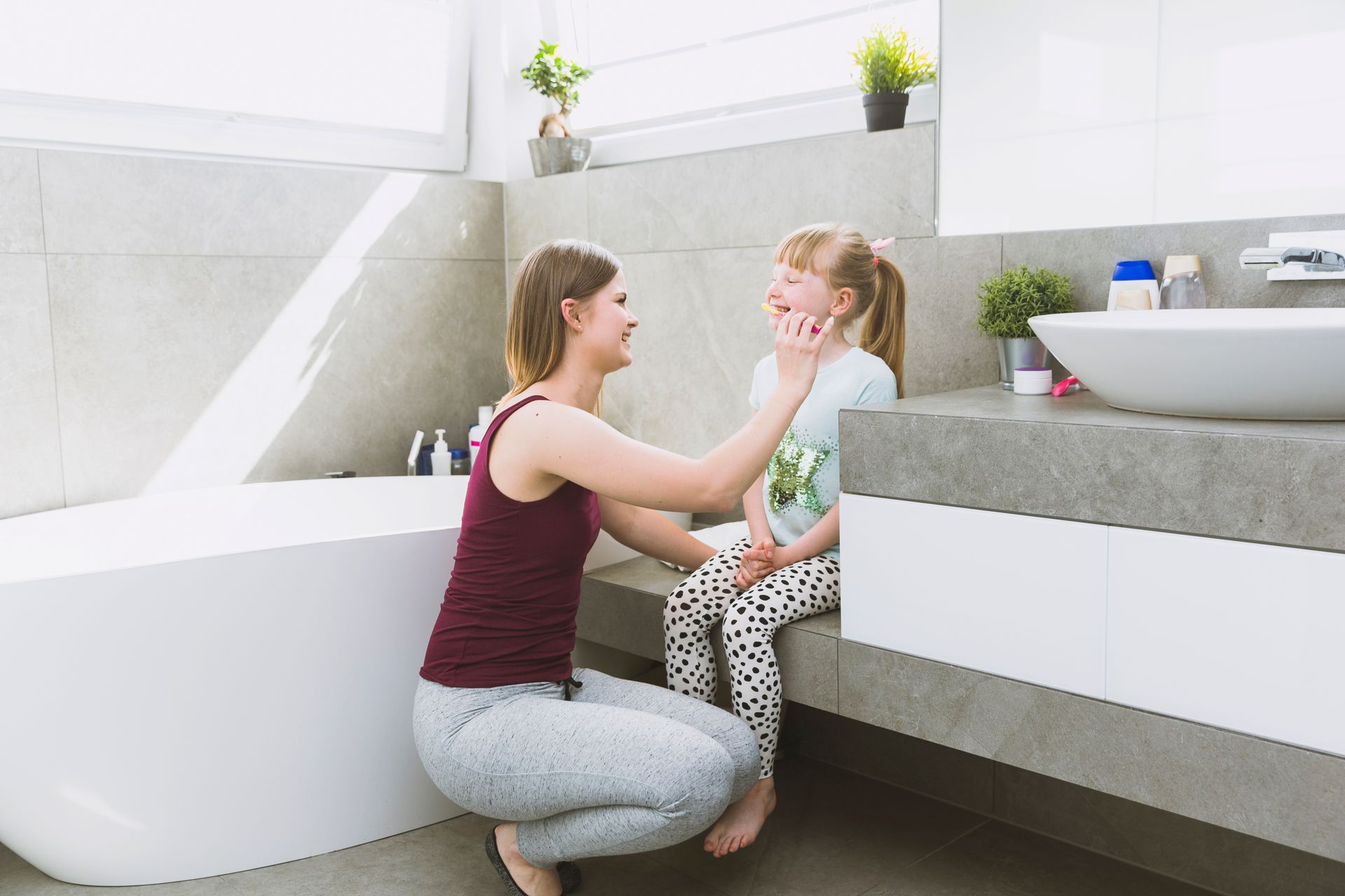 Woman and child in a modern bathroom, smiling. Woman kneels, touching child's face.