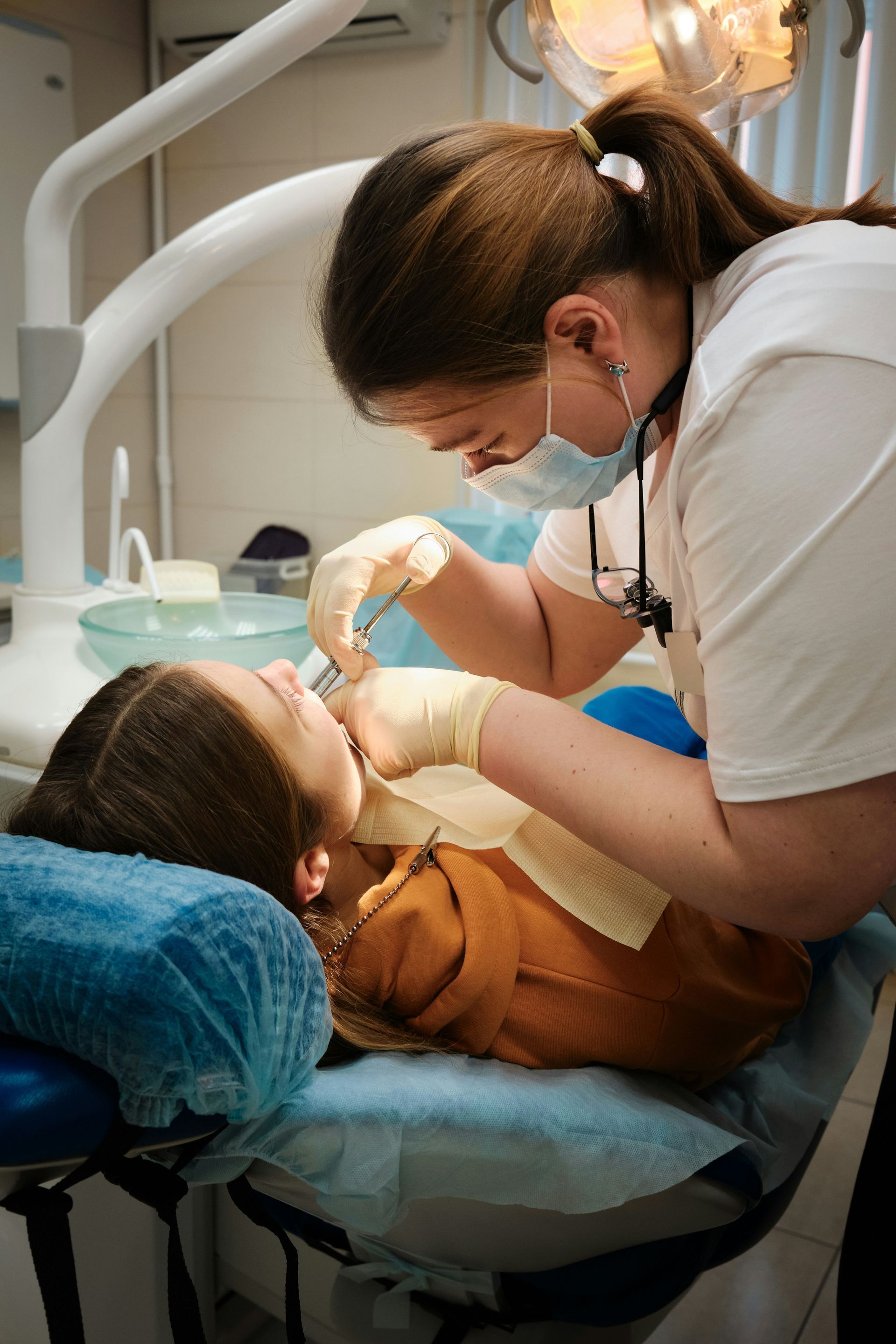 Dentist examining a patient's mouth in a dental office; dentist wears mask and gloves.