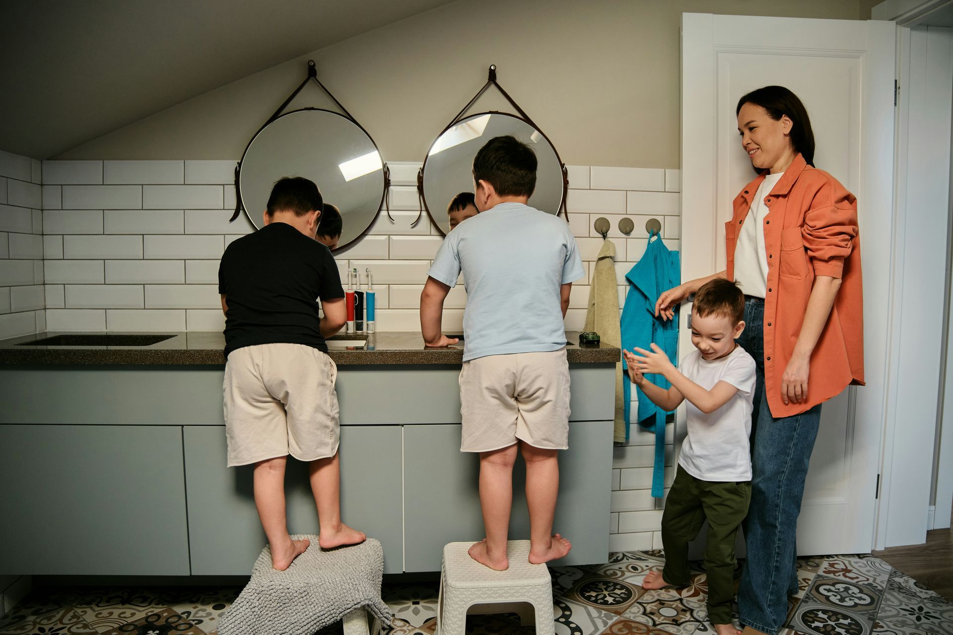 Woman supervises three children washing hands in a bathroom.