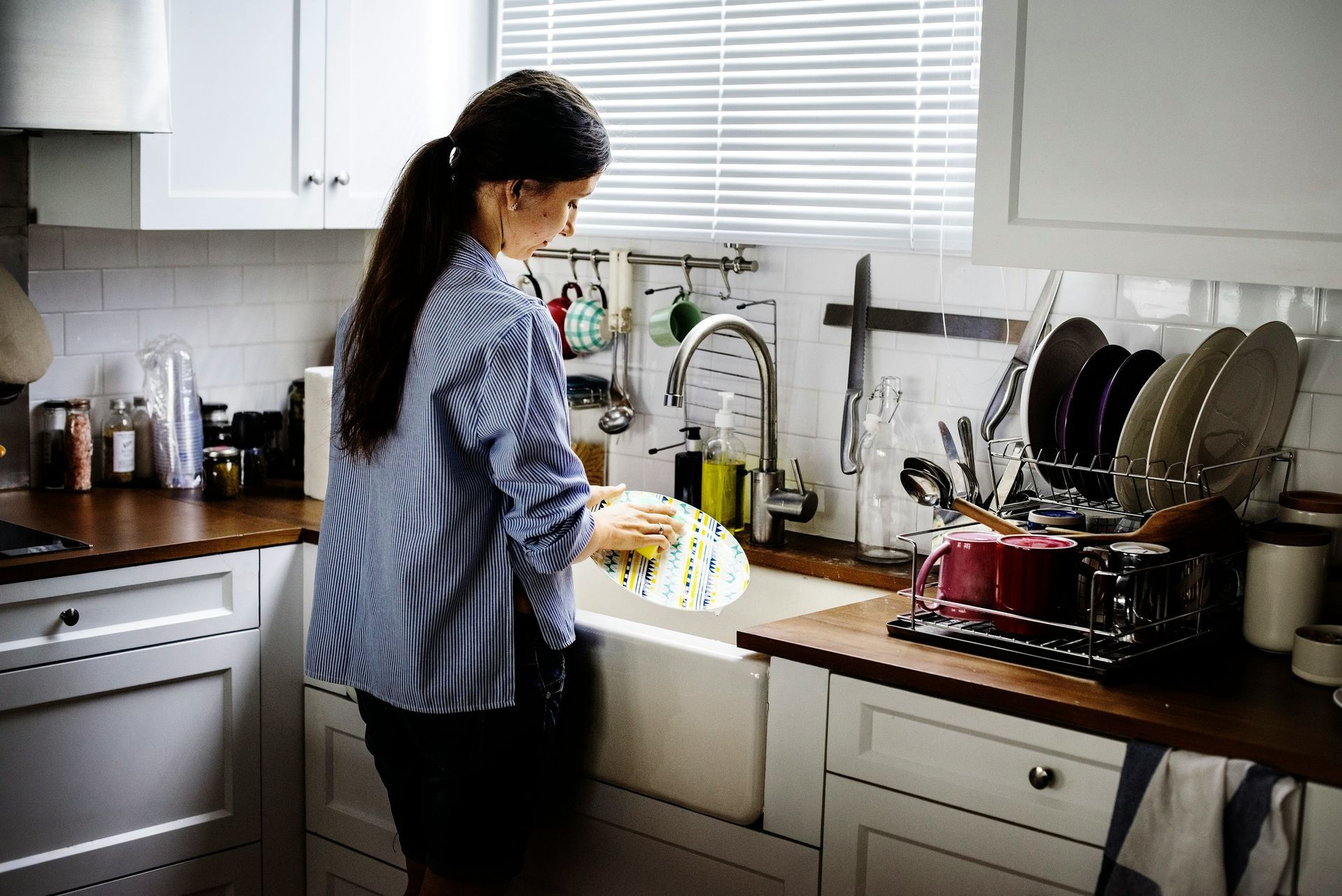 Woman washes a dish in a white kitchen sink.