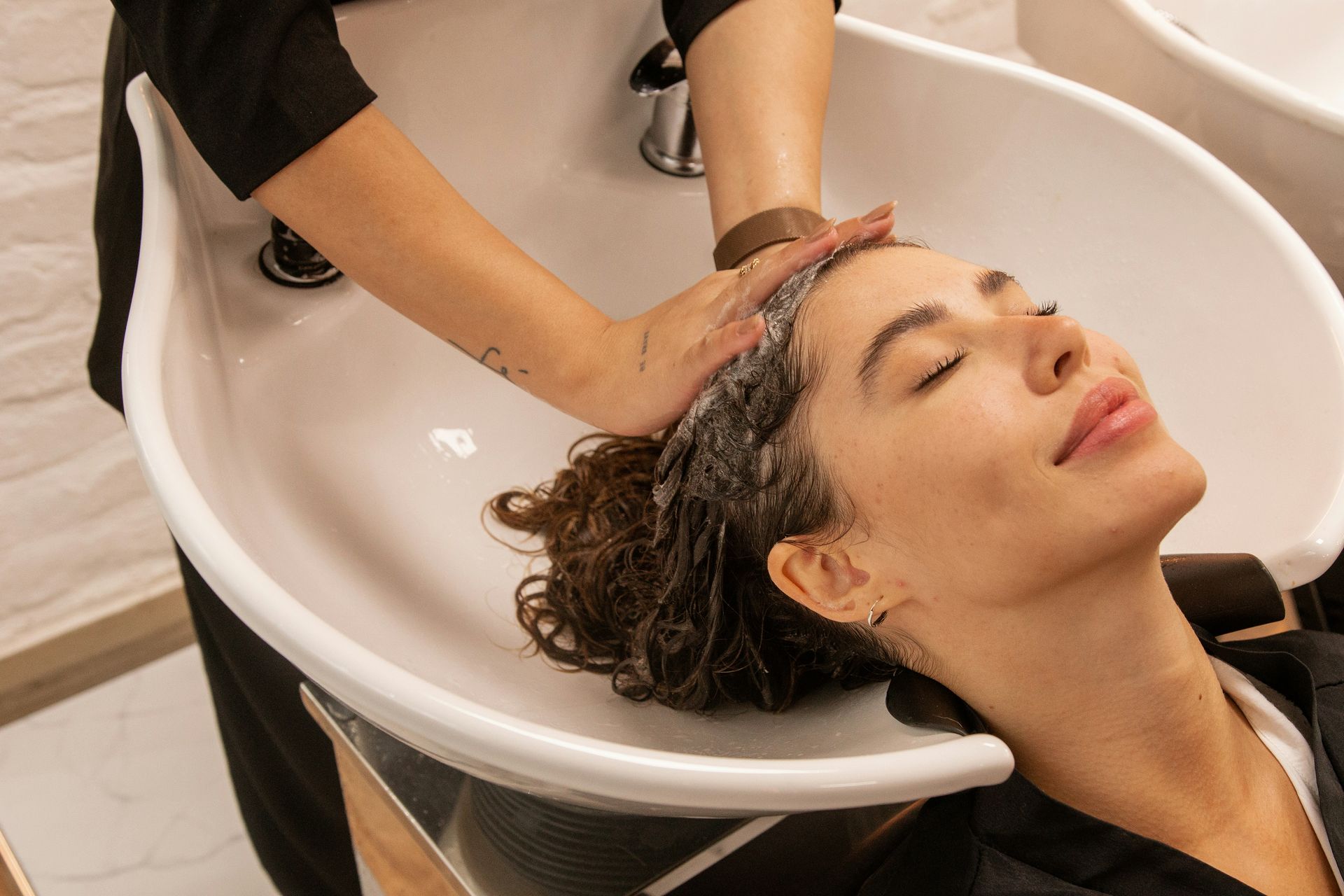 Woman getting her hair washed at a salon, eyes closed, head in a sink.