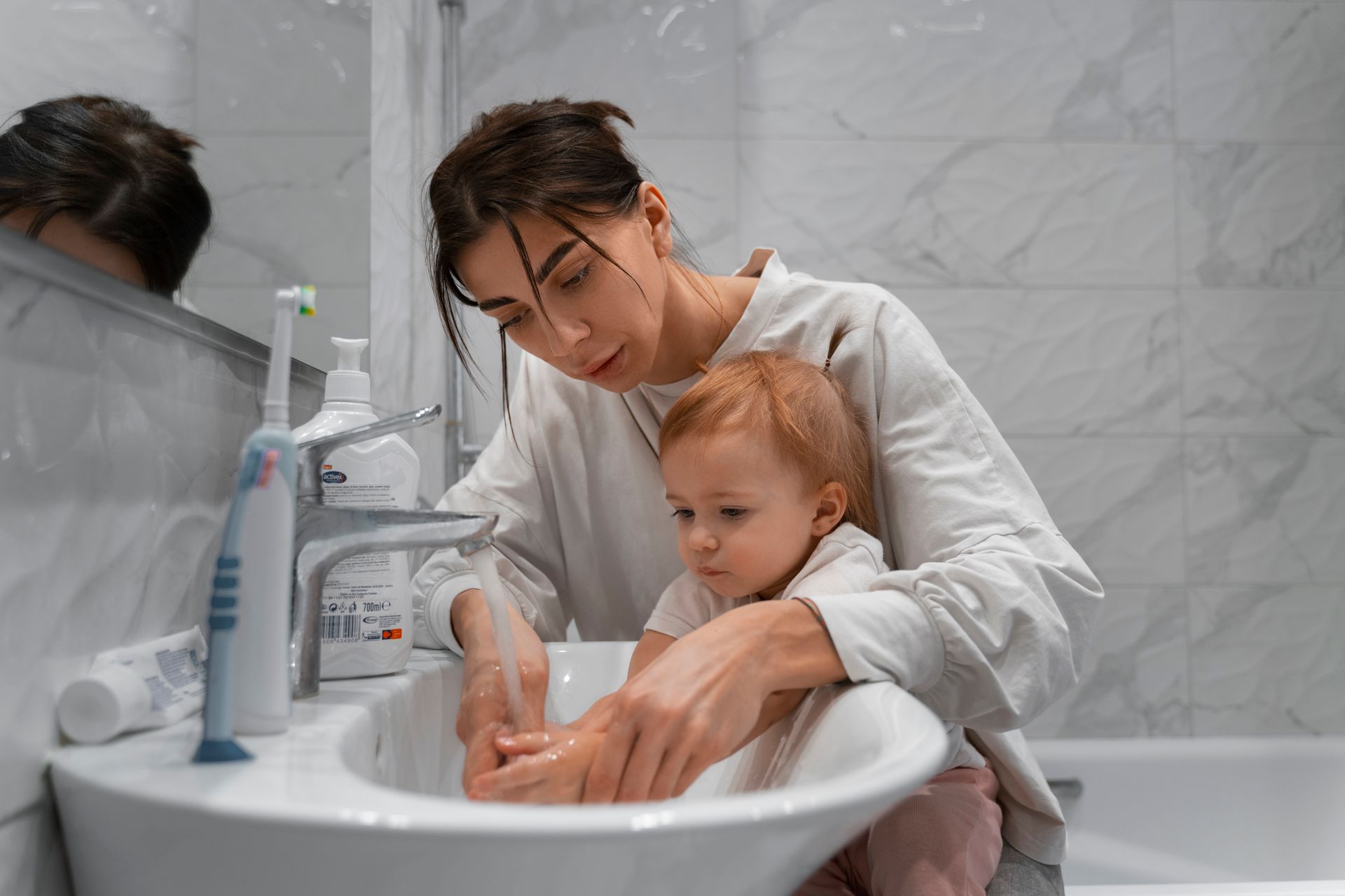 Woman washes a toddler's hands in a bathroom sink.