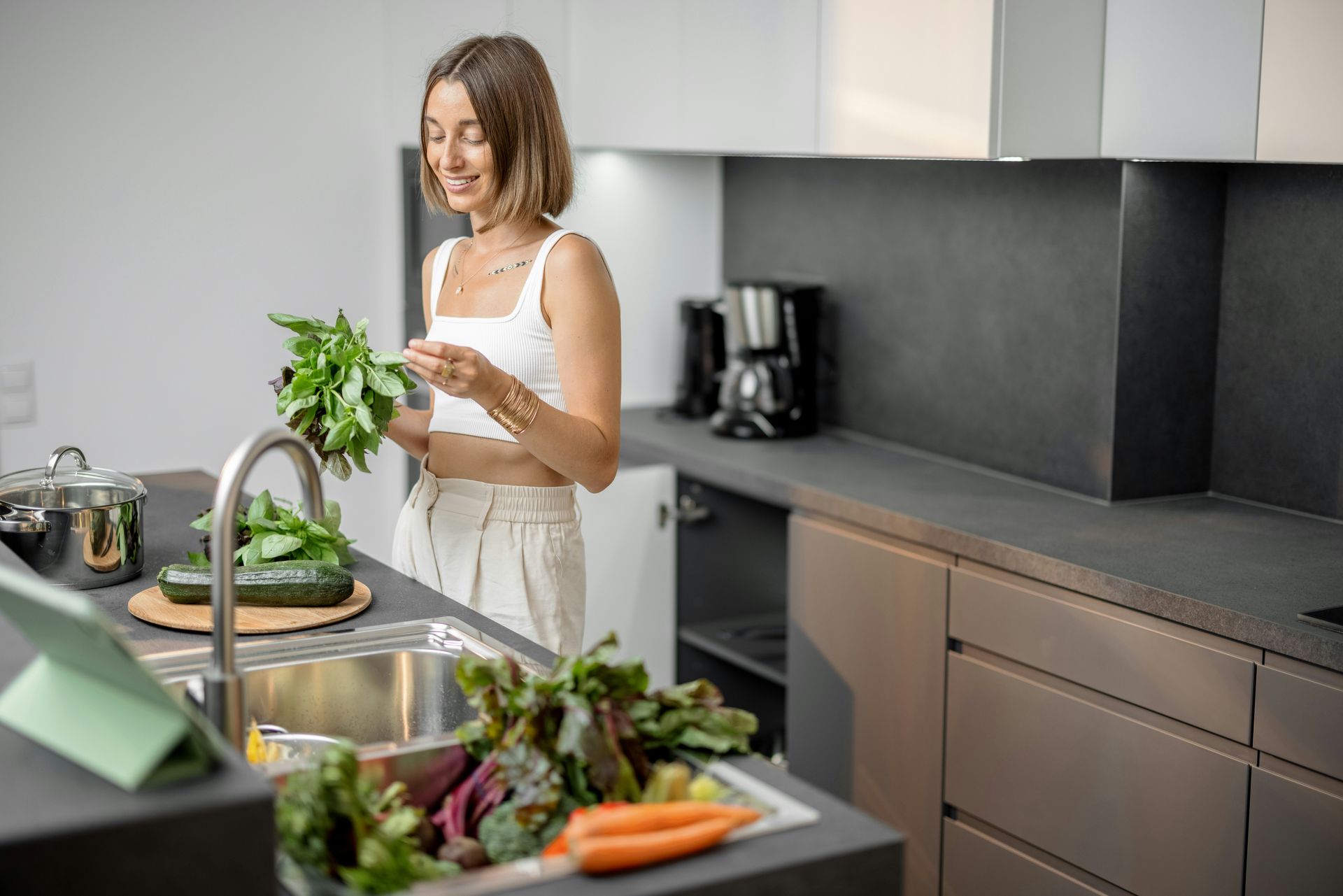 Woman in a modern kitchen preparing vegetables at the sink, smiling.