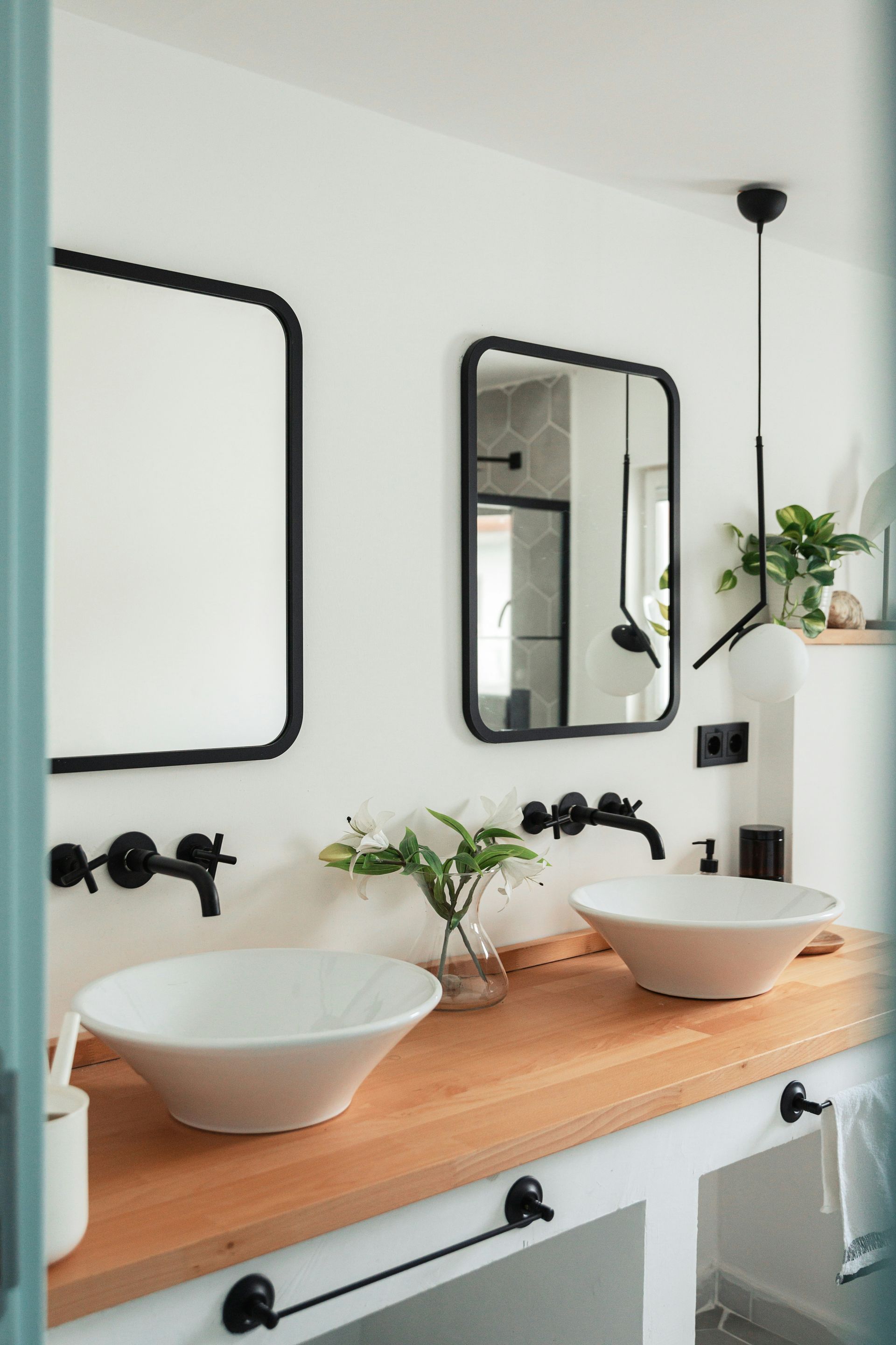 Bathroom with two white bowl sinks on a wood countertop, black faucets, mirrors, and a plant.