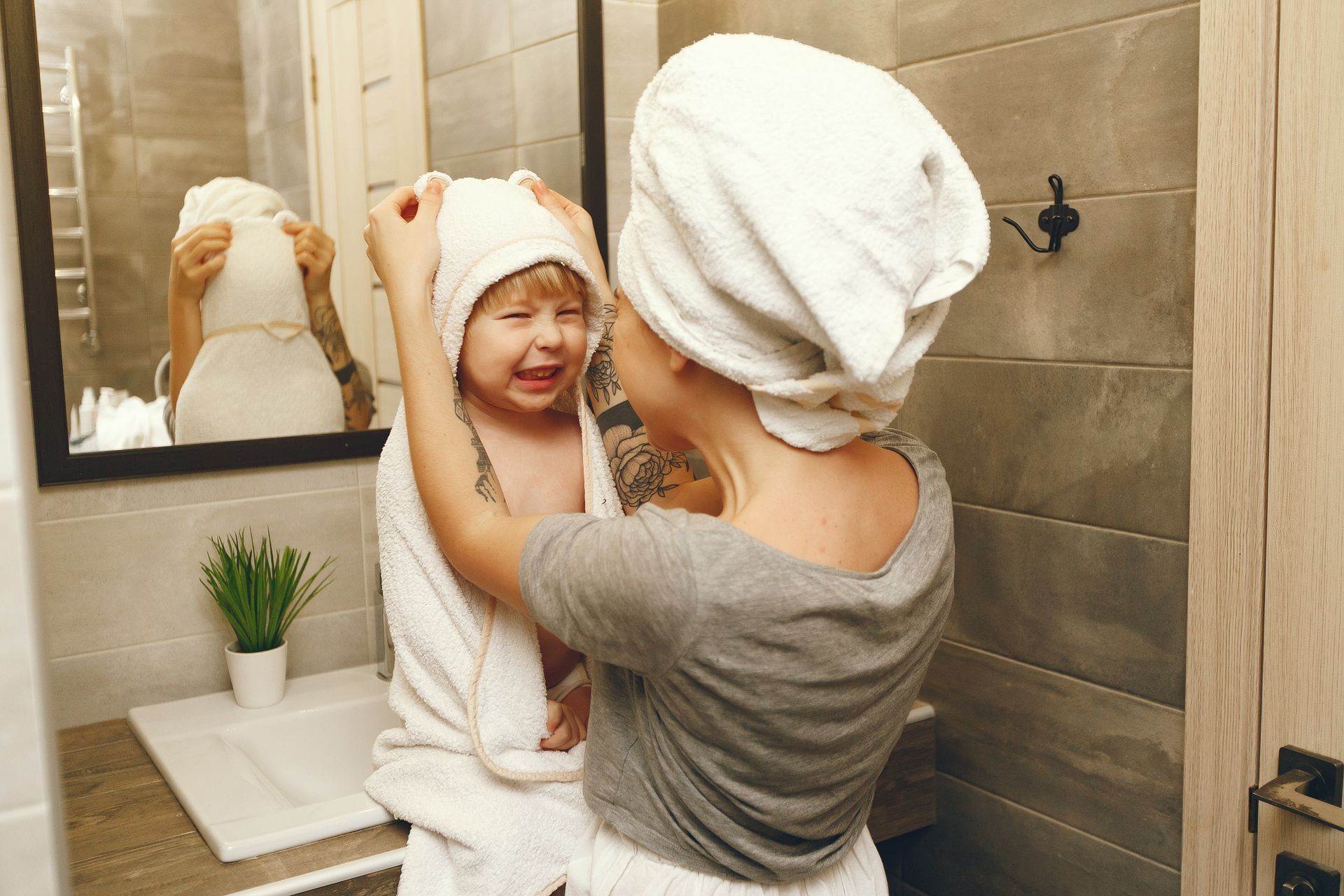 Woman drying child's hair with a towel in a bathroom. Child is crying. Mirror in background.