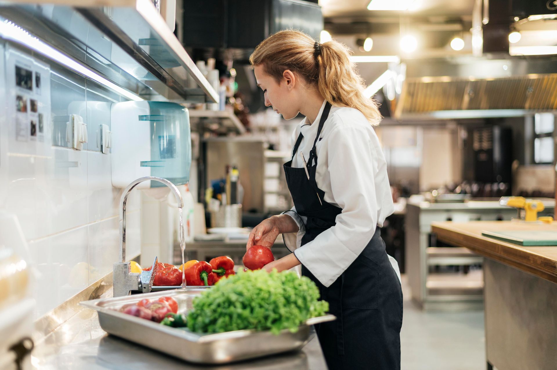 Chef in black apron washing vegetables in a commercial kitchen.