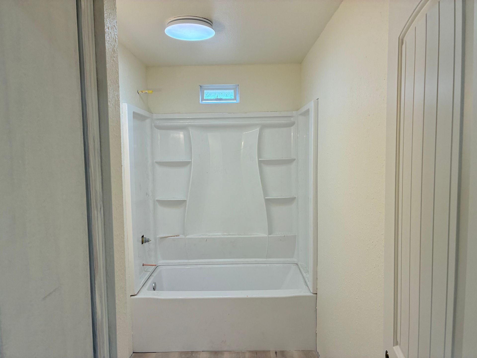 Small beige bathroom with a white shower/tub combination and skylight above