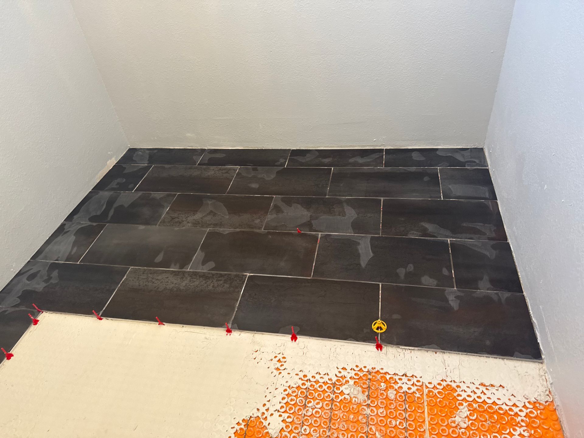 Small tiled alcove with dark floor tiles and unfinished white walls, with a light-colored floor edge in front.