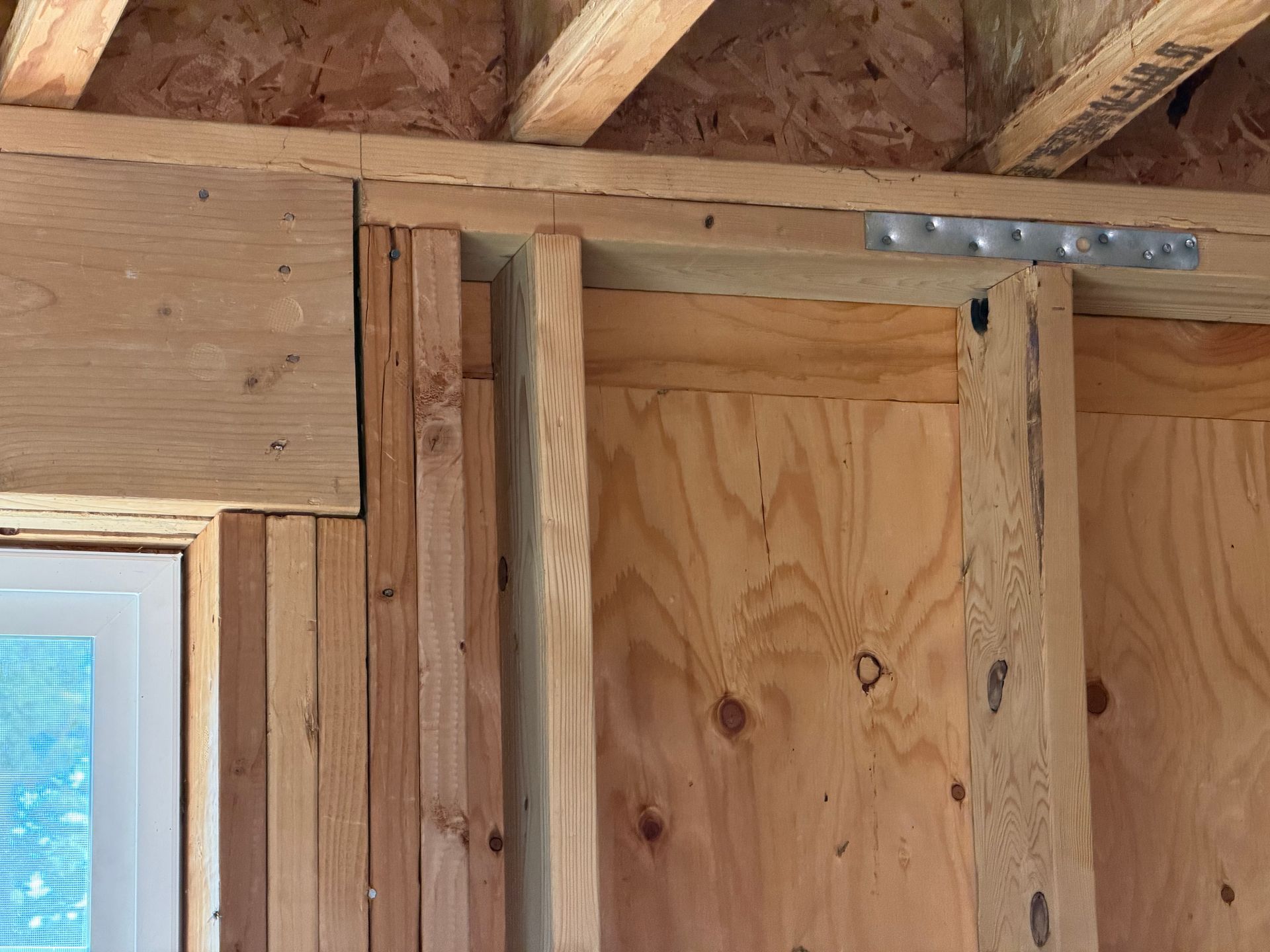 Wood-framed wall and door opening under exposed ceiling joists, with window trim on the left.