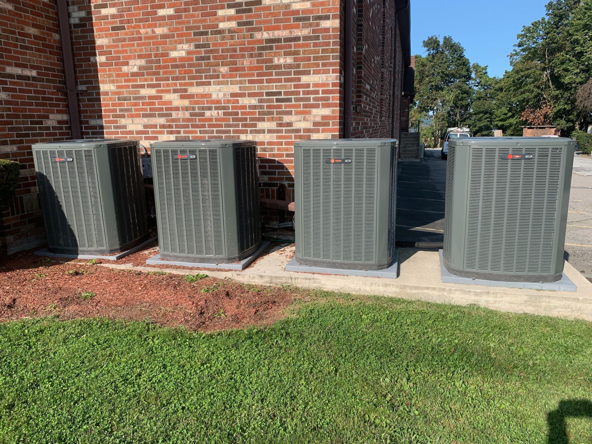 Three air conditioners are sitting on the sidewalk in front of a brick building.