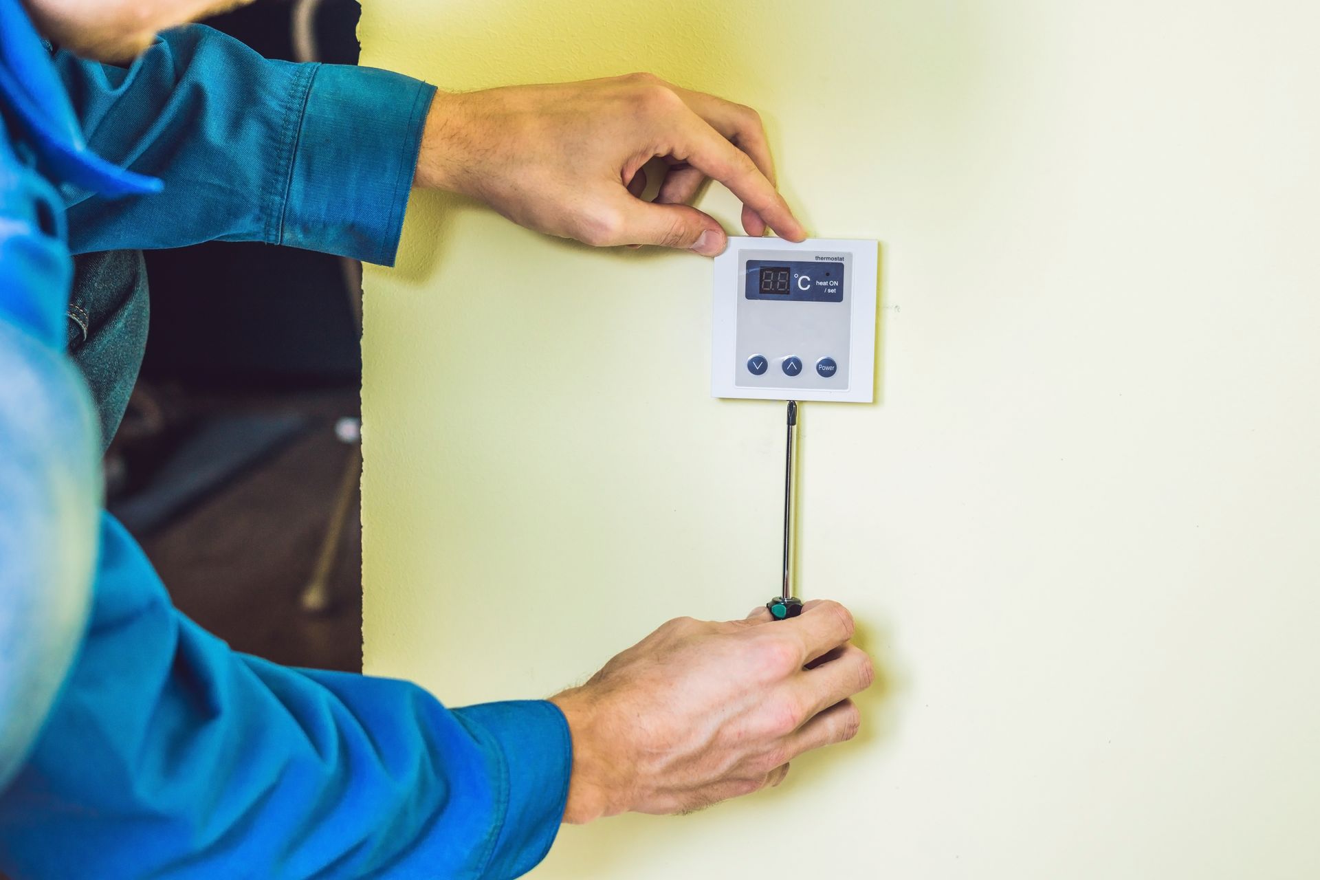 A man is installing a thermostat on a wall with a screwdriver.