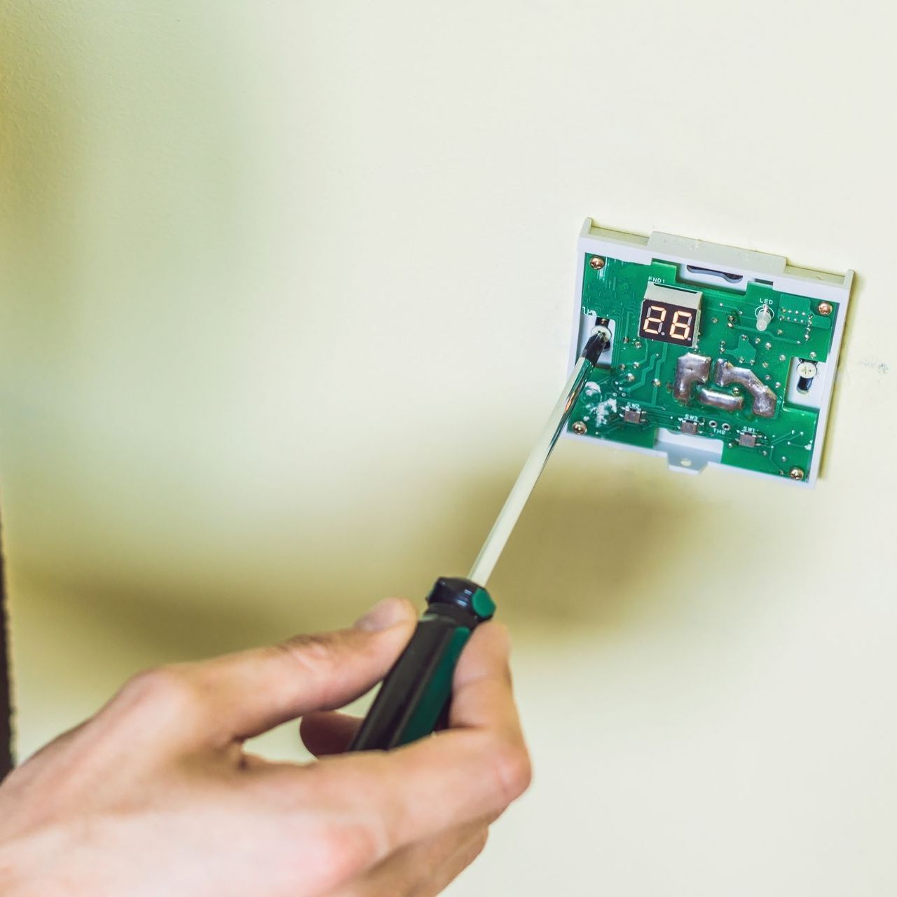 A person is fixing a thermostat with a screwdriver.