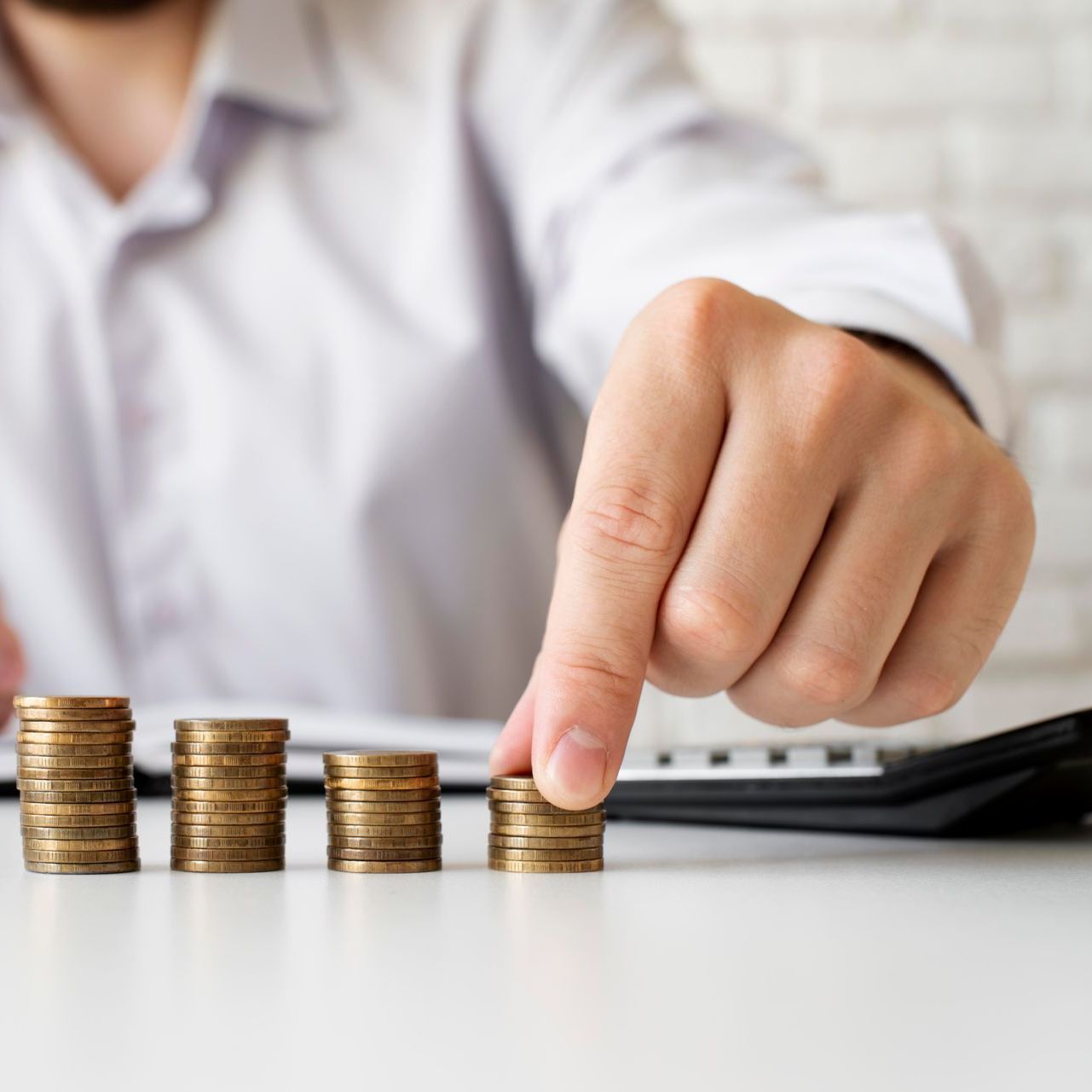 A man is stacking coins on a table while using a calculator.