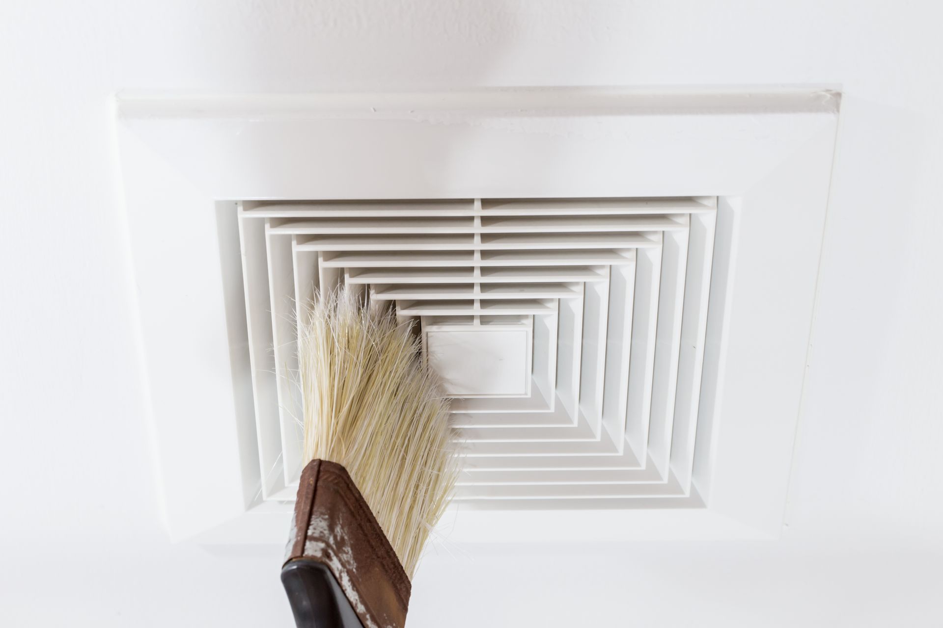 A person is cleaning an air vent with a brush.