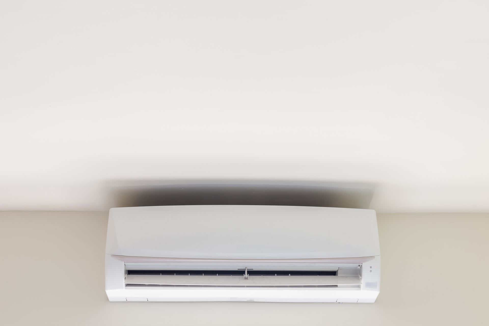 A white air conditioner is hanging on a white wall.