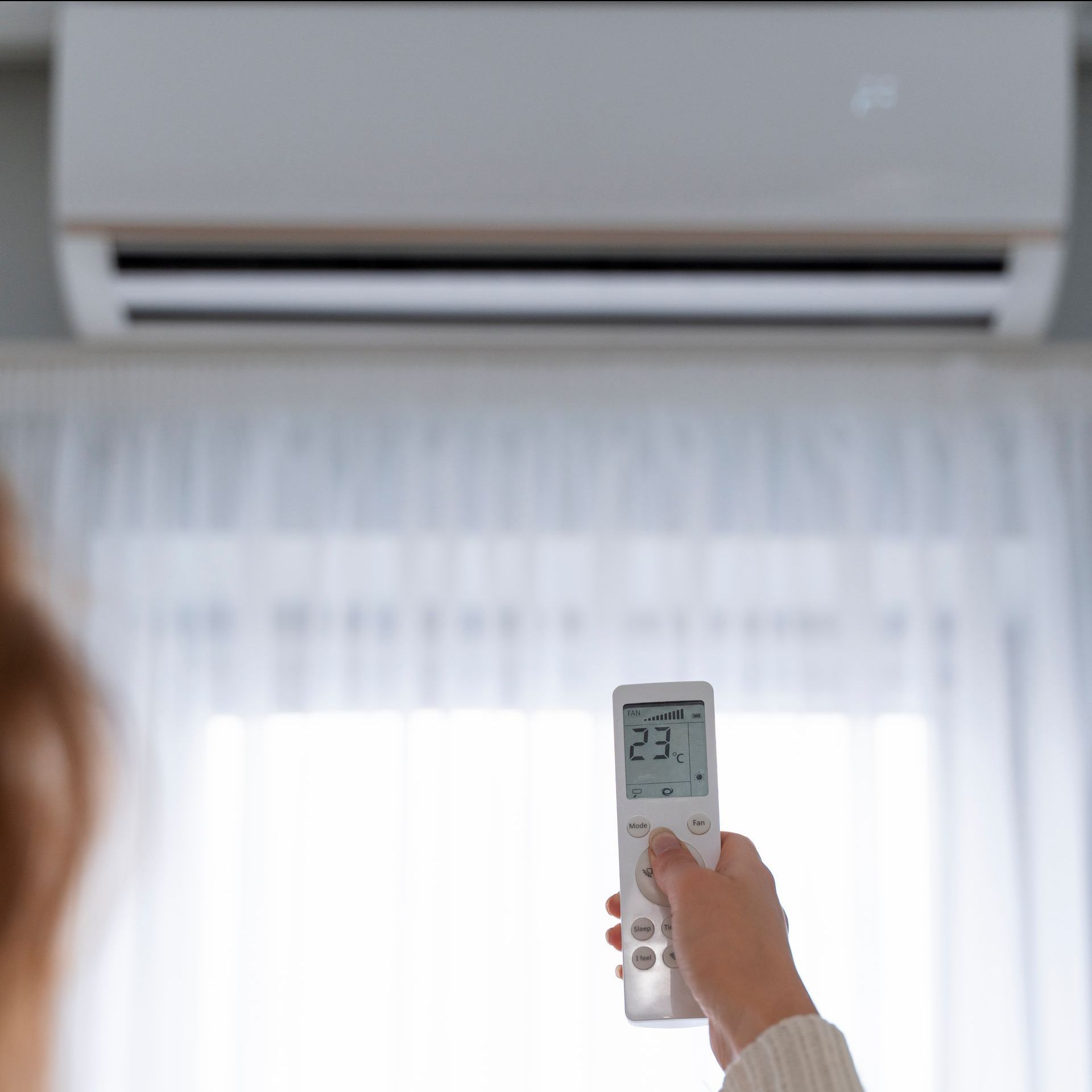 A woman is holding a remote control in front of an air conditioner.