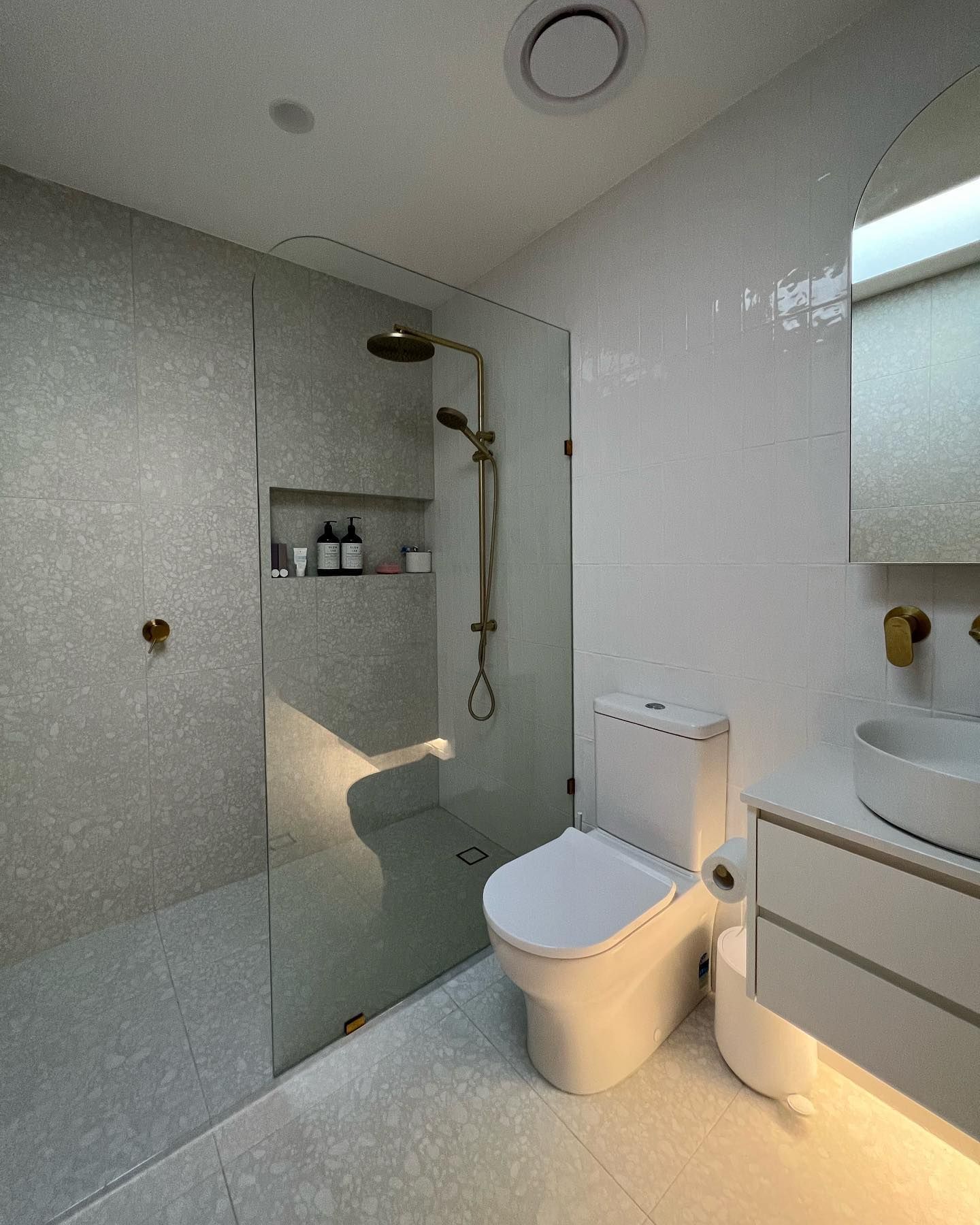 Modern bathroom with grey tiled shower, glass door, white toilet, and gold fixtures  — J & H Plumbing and Gas in Holt, ACT