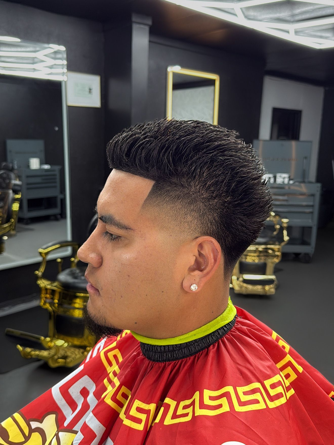 Man with textured hair and a skin fade haircut in a barbershop, wearing a red cape.