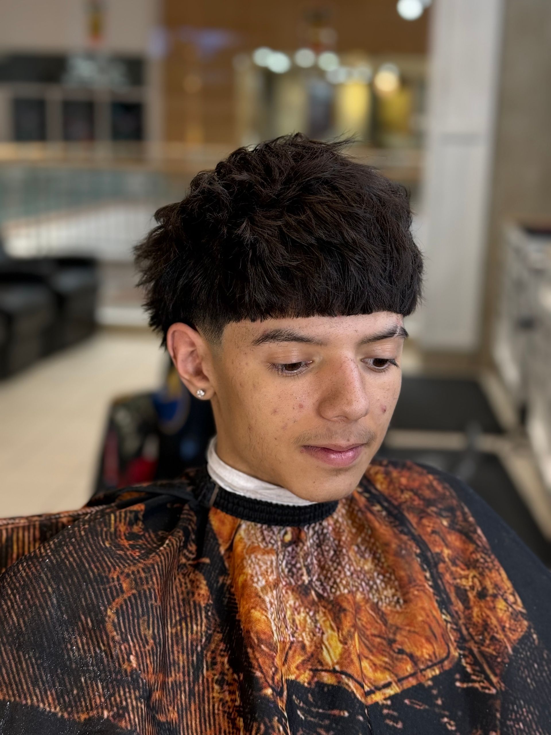 A young person with a textured hairstyle, wearing a salon cape.