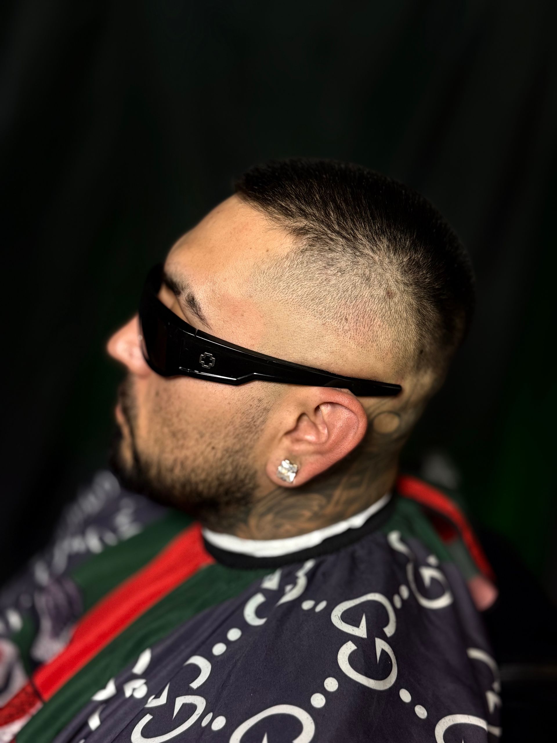Person with a faded haircut, wearing sunglasses, and a Gucci barber cape.
