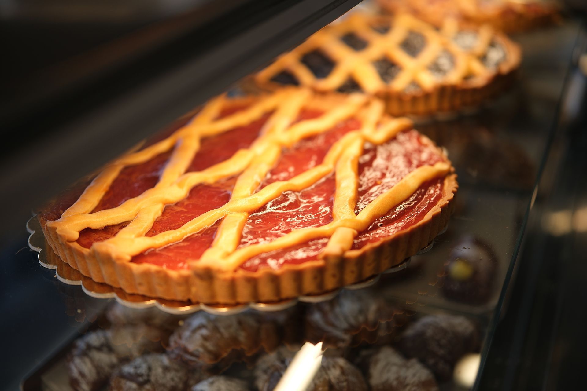 Crostatine di marmellata di fragole con crosta a reticolo esposte in una teca di vetro.