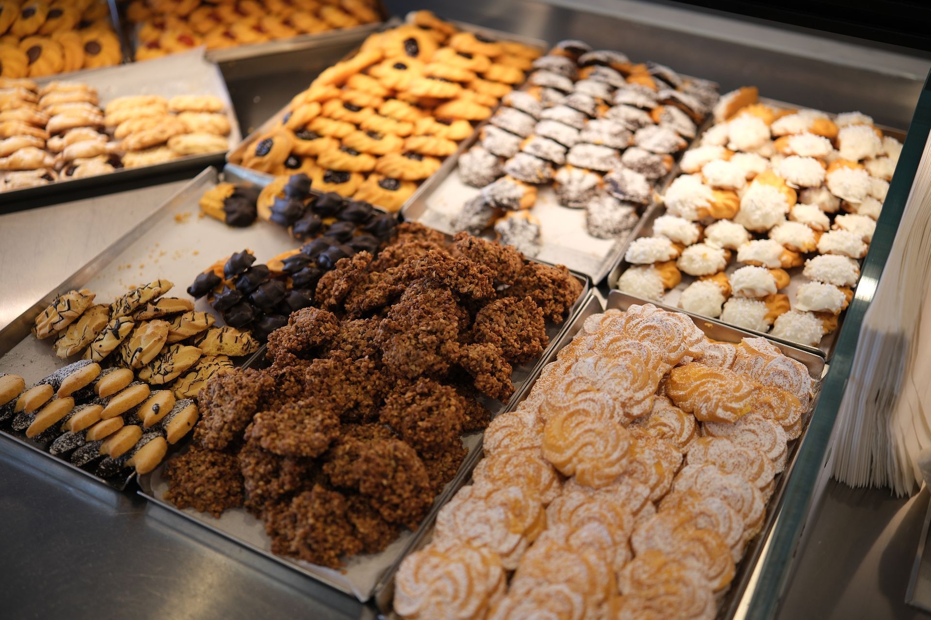 Varietà di biscotti esposti in una vetrina da pasticceria: cioccolato, zucchero a velo e forme assortite.