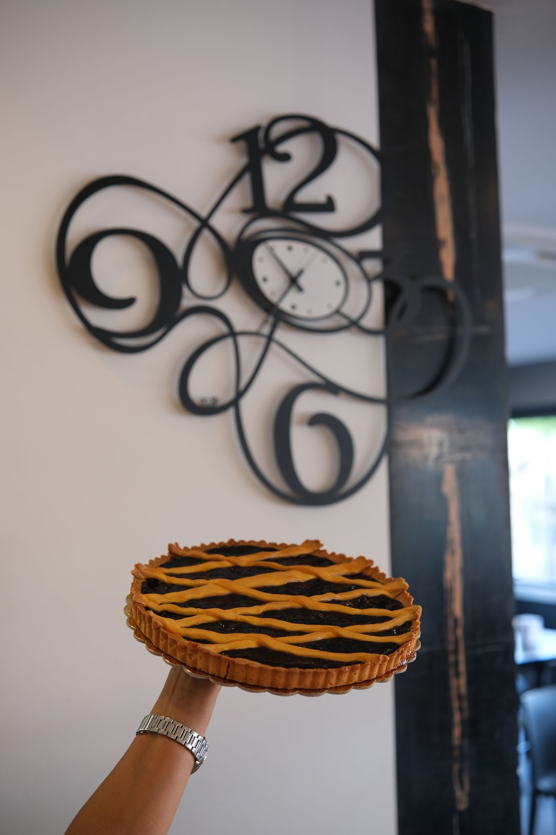 Mano che regge una torta con una crosta a grata davanti a un orologio da parete decorativo.