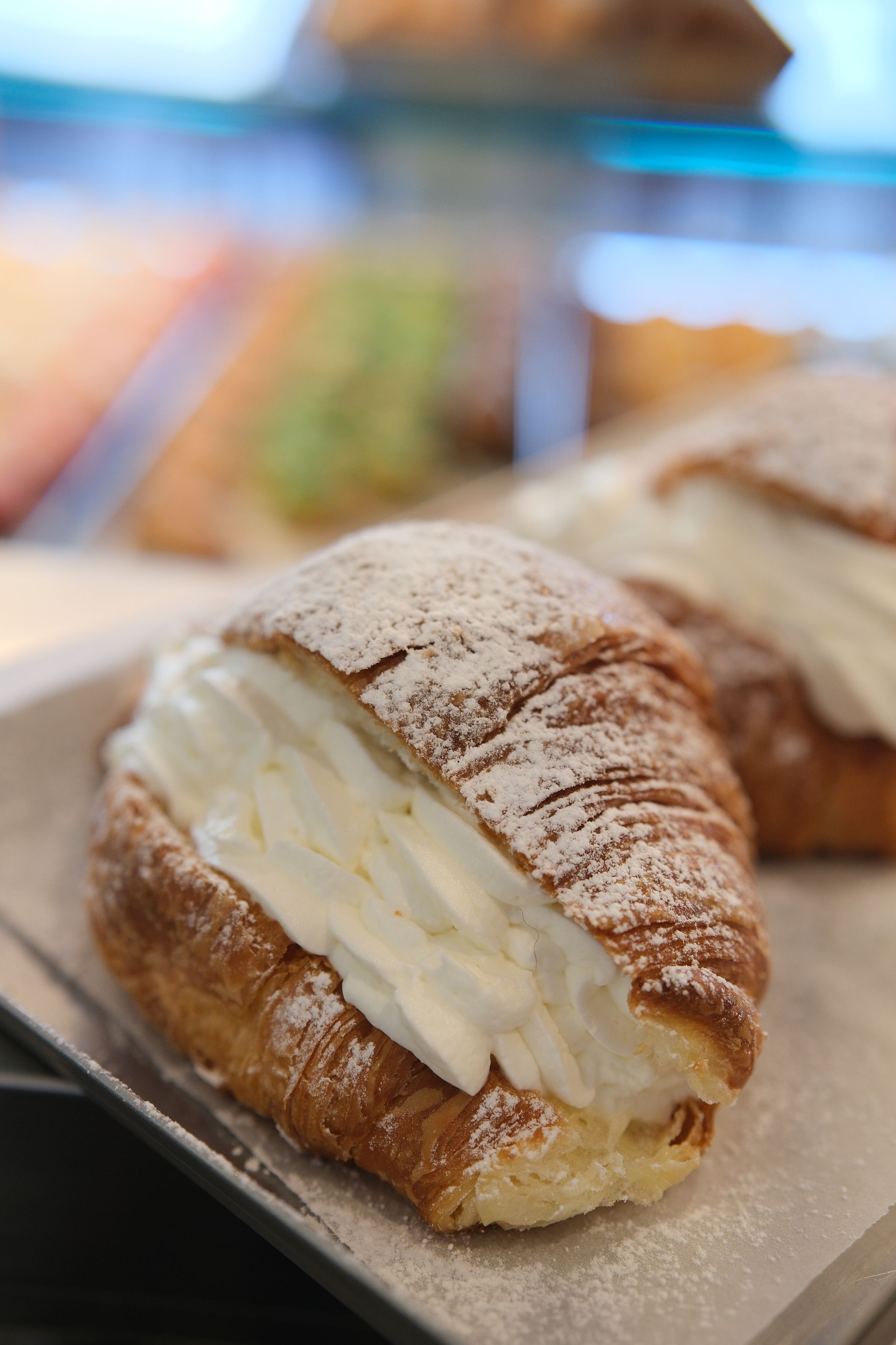 Croissant farcito con panna montata, spolverato con zucchero a velo, su carta da forno.