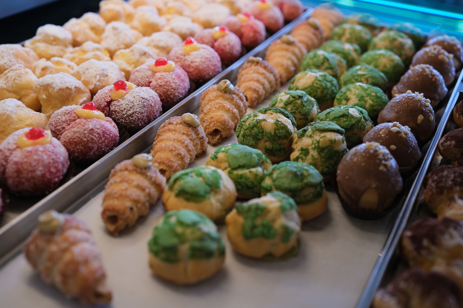 Pasticcini di vari colori e forme disposti su vassoi, pronti per essere esposti.
