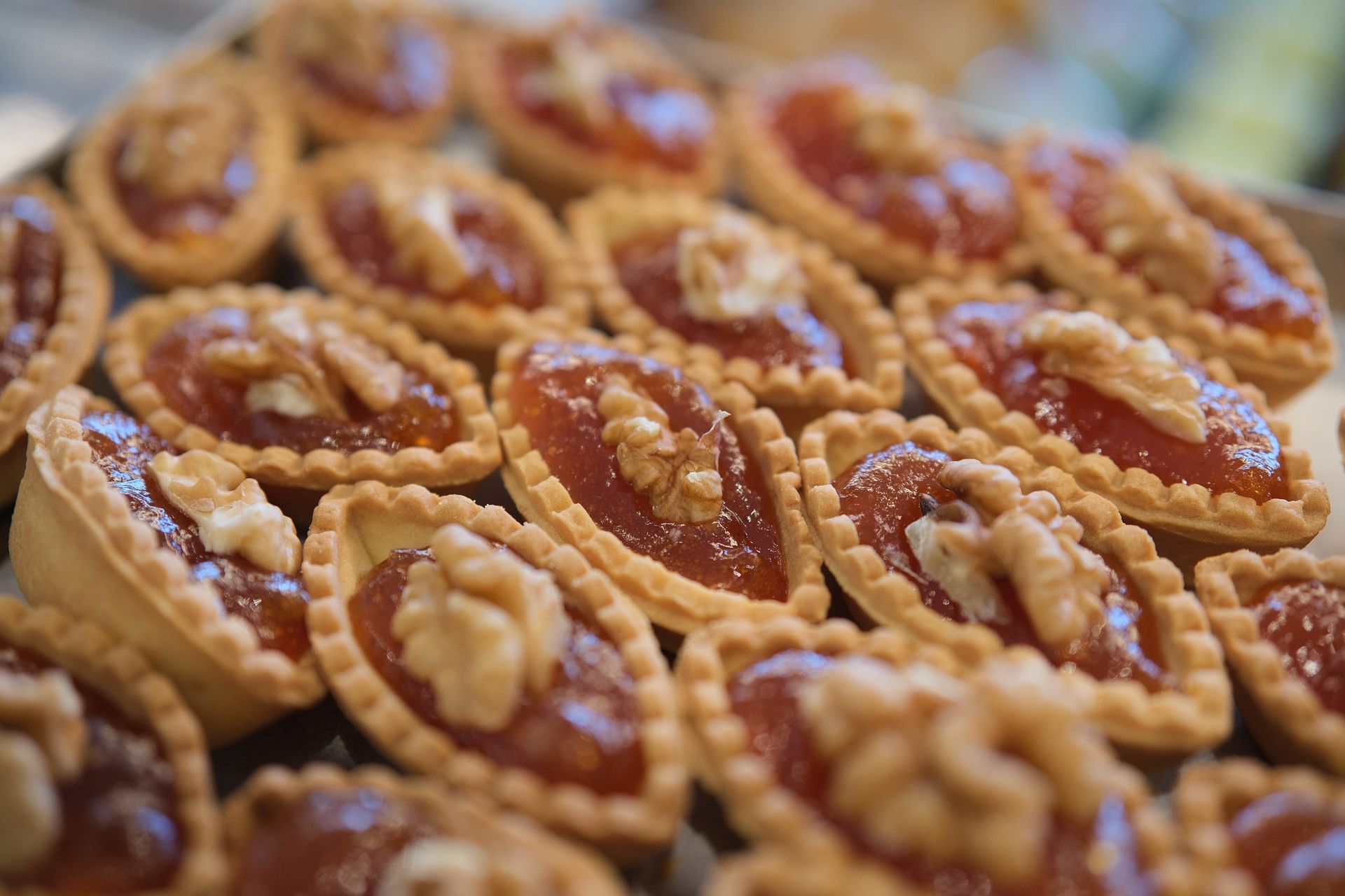 Piccole crostatine ripiene di marmellata e guarnite con noci, disposte su un vassoio.