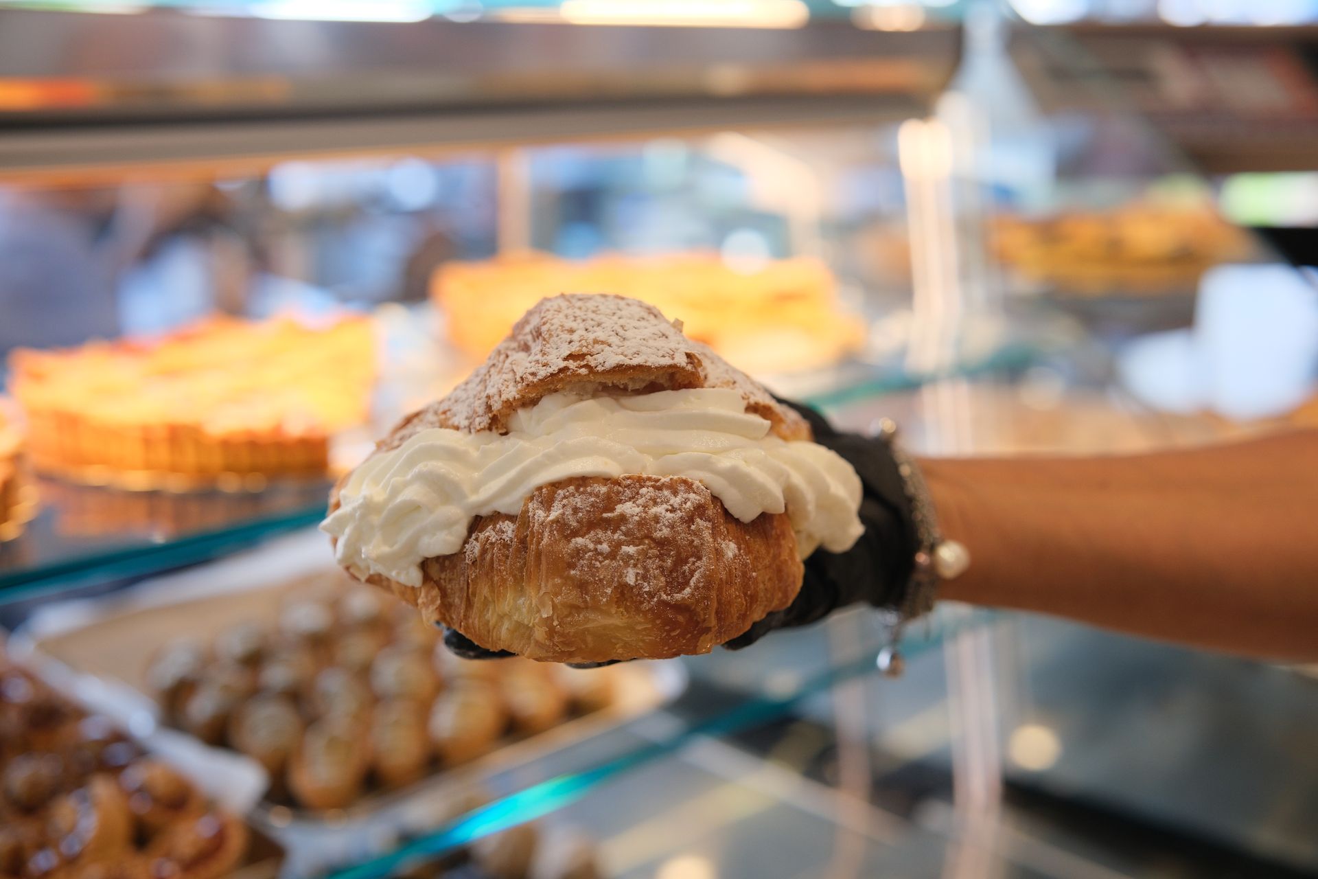 Una mano che tiene un croissant con panna montata, spolverato con zucchero a velo, espositore da pasticceria.