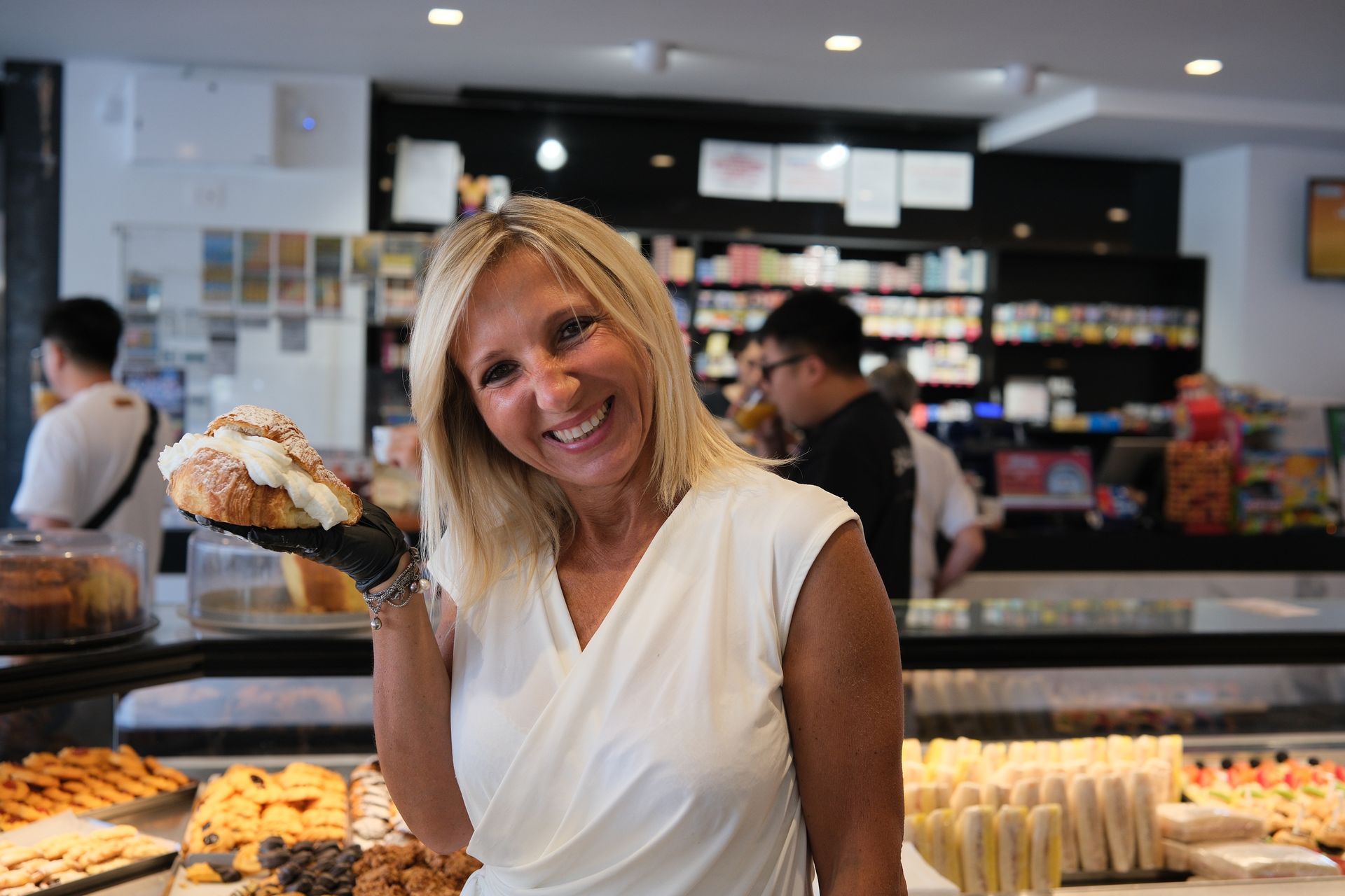 Una donna bionda sorride, tenendo in mano un dolce, in una panetteria.