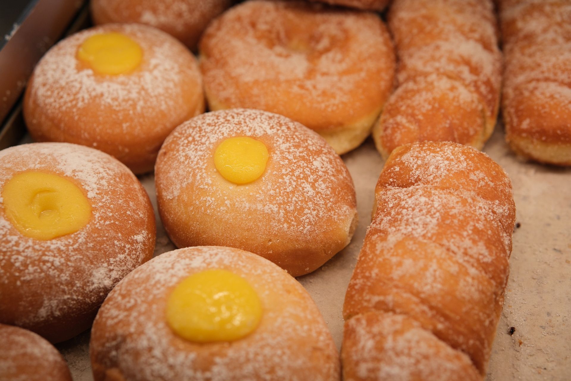 Ciambelle con zucchero a velo, alcune ripiene di crema pasticcera gialla, esposte in una vetrina di pasticceria.