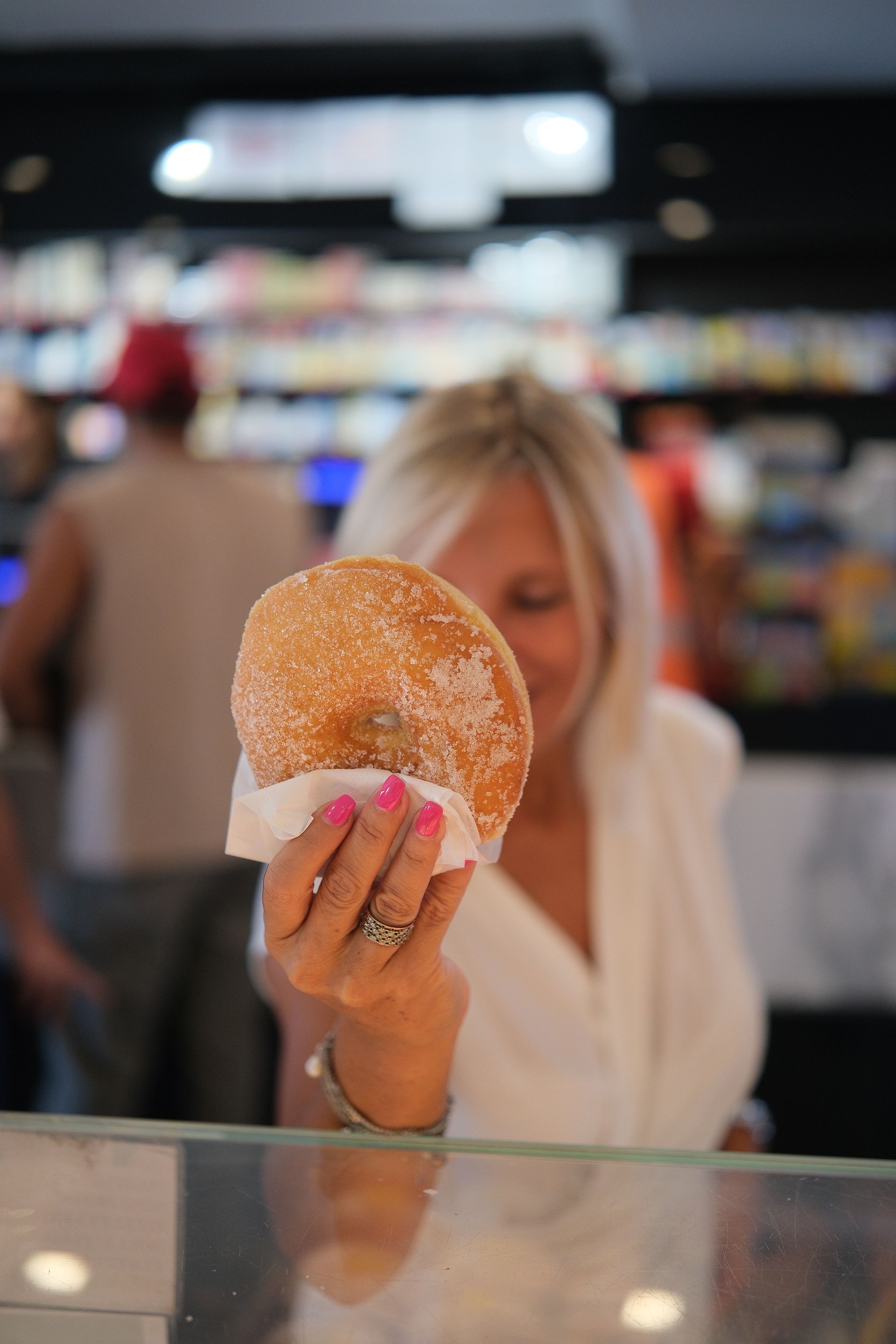grande ciambella ricoperta di zucchero, in una pasticceria. Unghie rosa, capelli biondi.