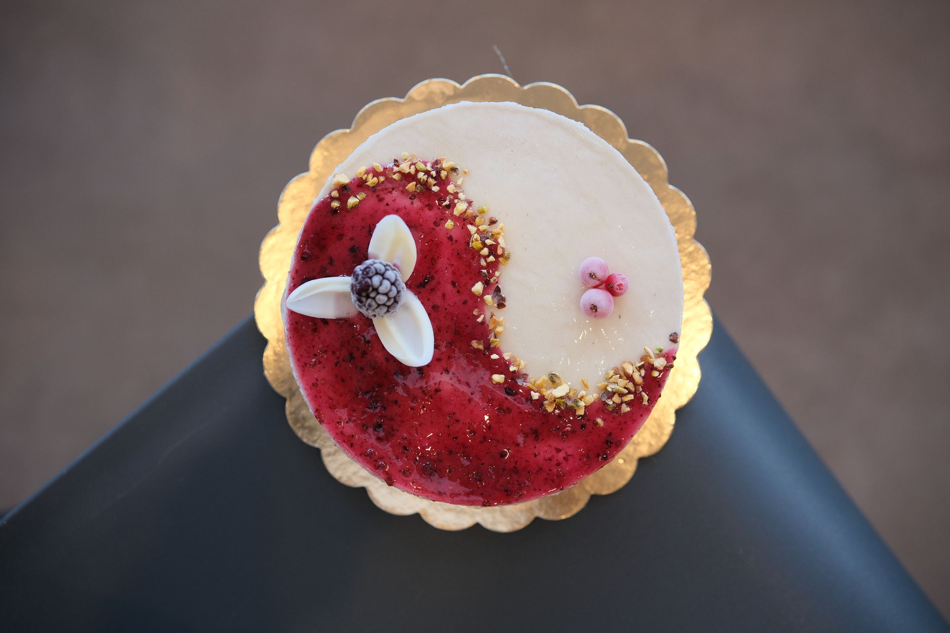 Una torta rotonda a forma di yin-yang con sezioni rosse e bianche, decorata con fiori commestibili e granelli dorati.