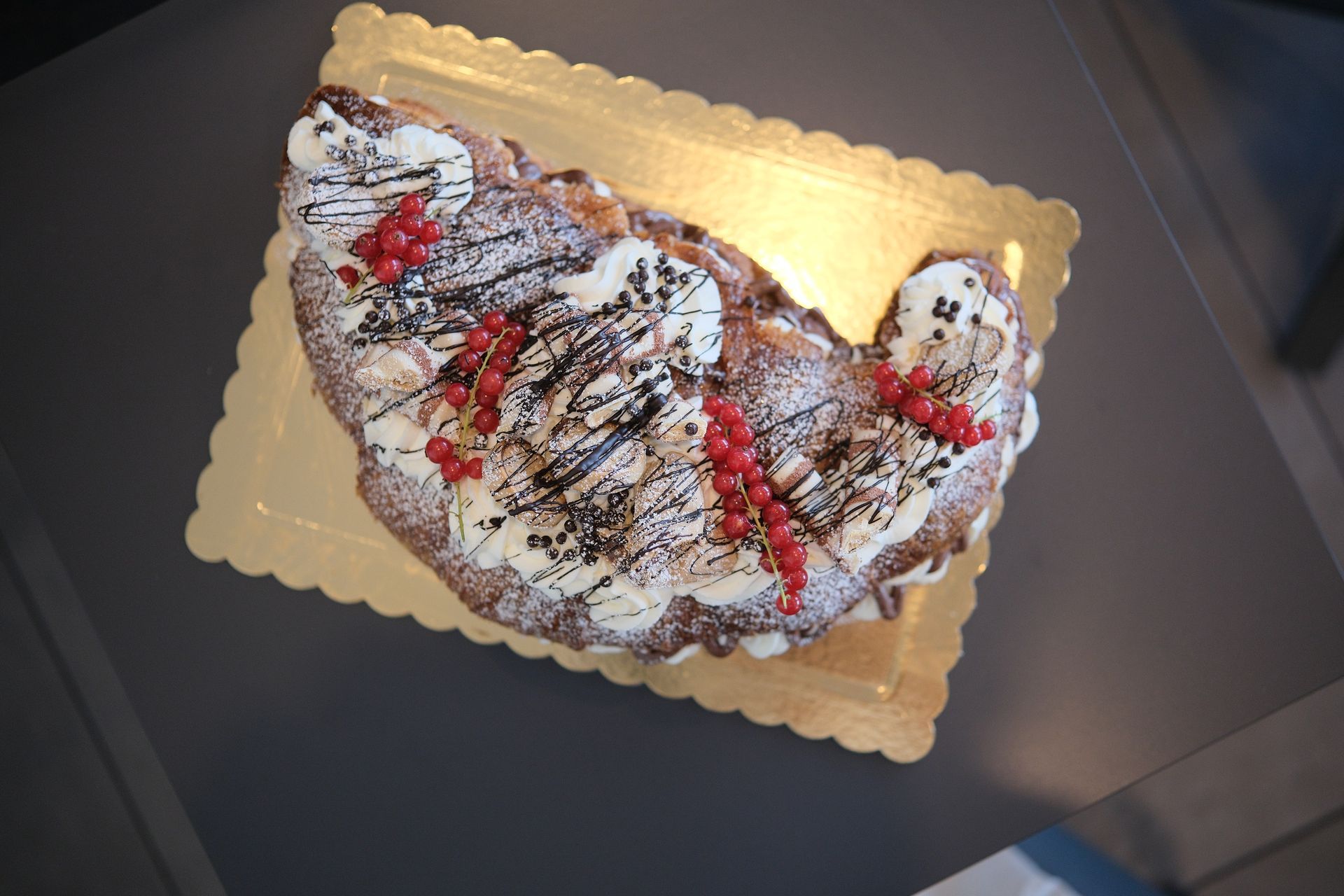 Un grande dolce ripieno di crema, con frutti rossi e gocce di cioccolato, servito su un vassoio dorato.