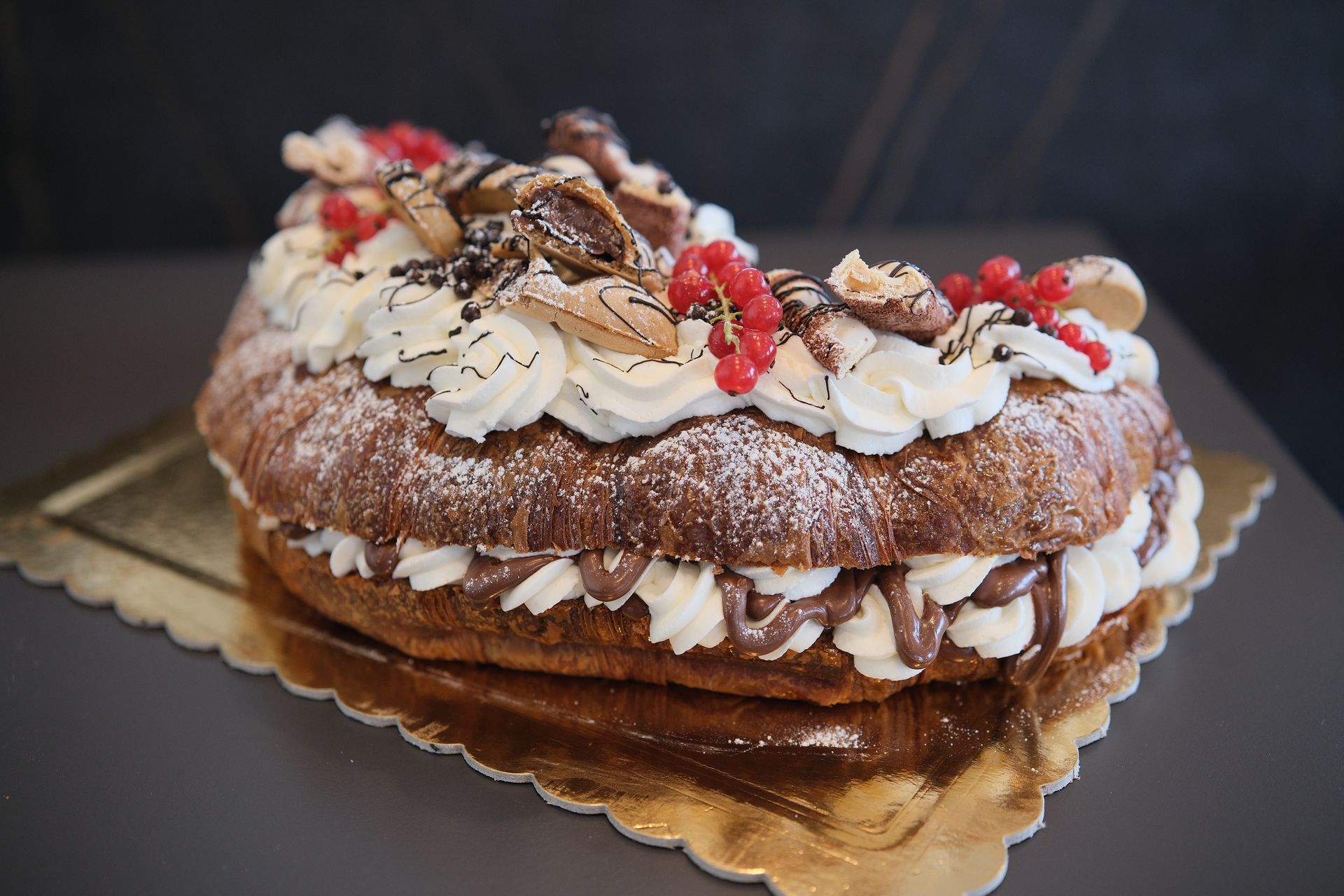 Cornetto farcito con panna montata, spolverato con zucchero a velo, su un piccolo piatto nero.