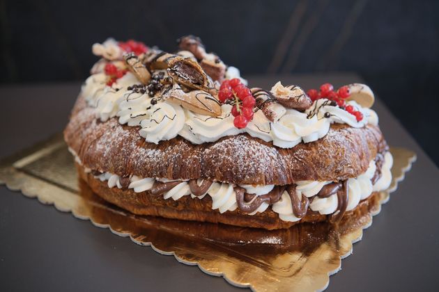 Cornetto farcito con panna montata, spolverato con zucchero a velo, su un piccolo piatto nero.