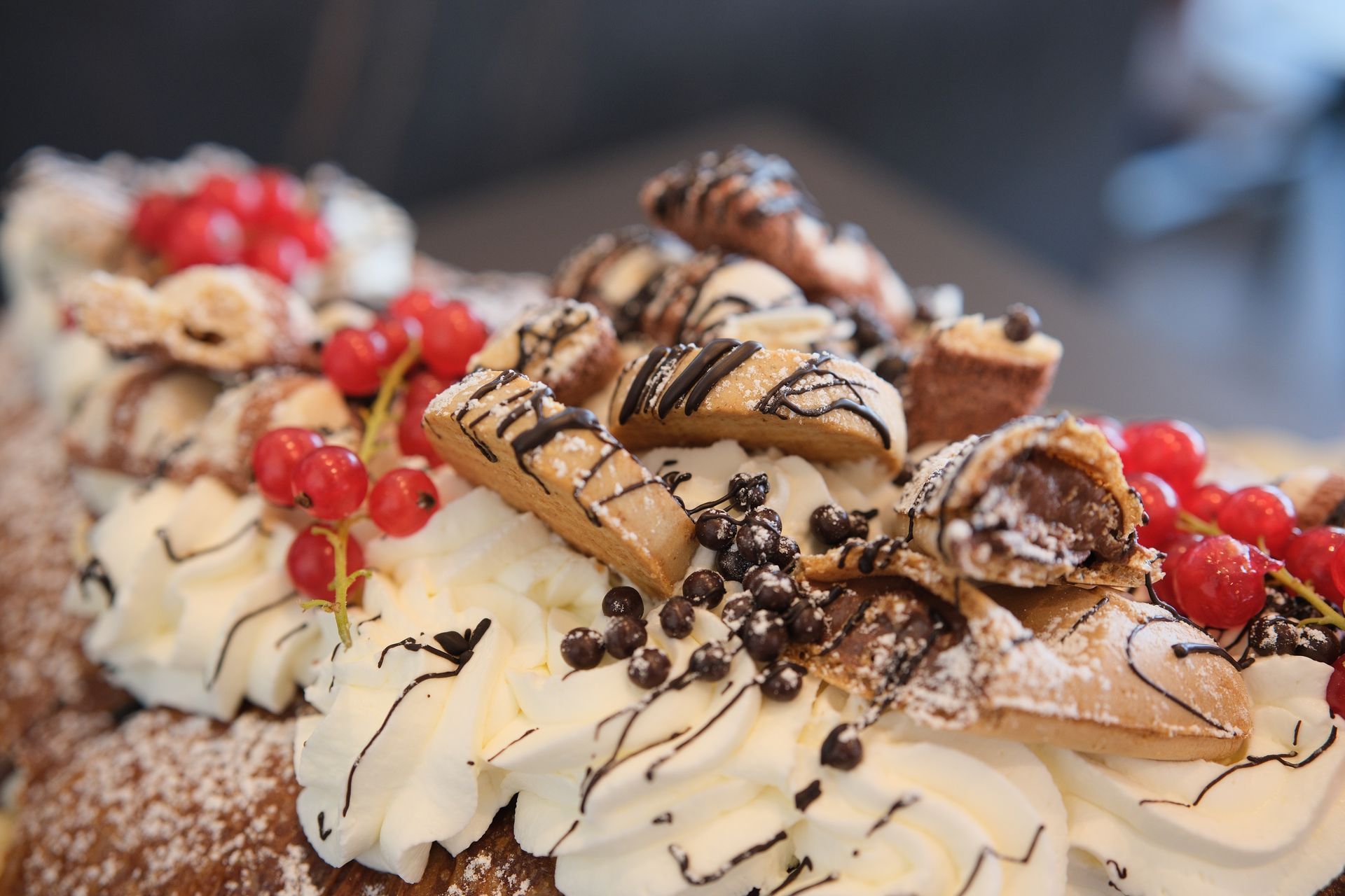 Primo piano di un dessert con panna montata, ribes rossi, gocce di cioccolato e pasticcini.