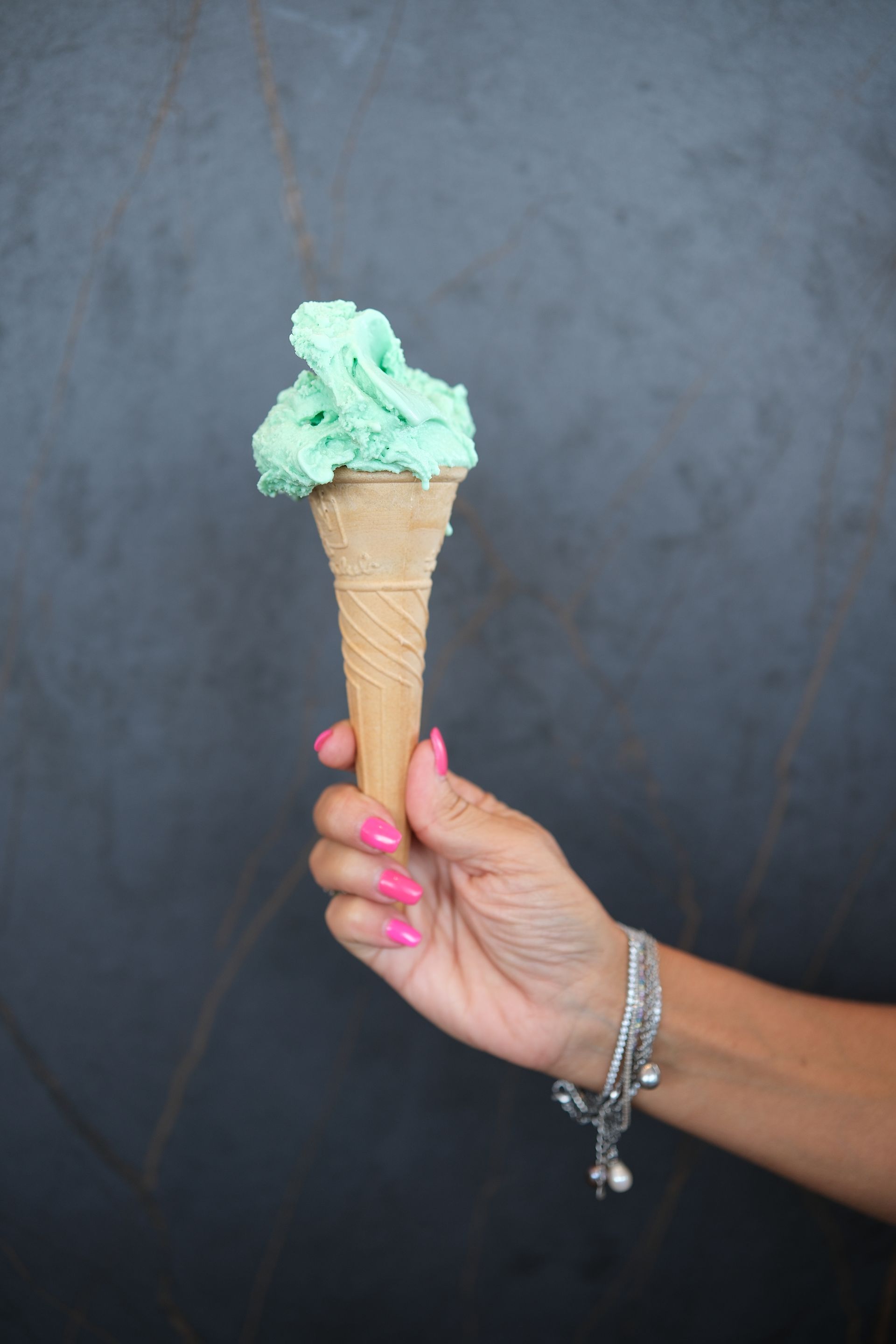 Mano che tiene un cono gelato verde menta su uno sfondo scuro.