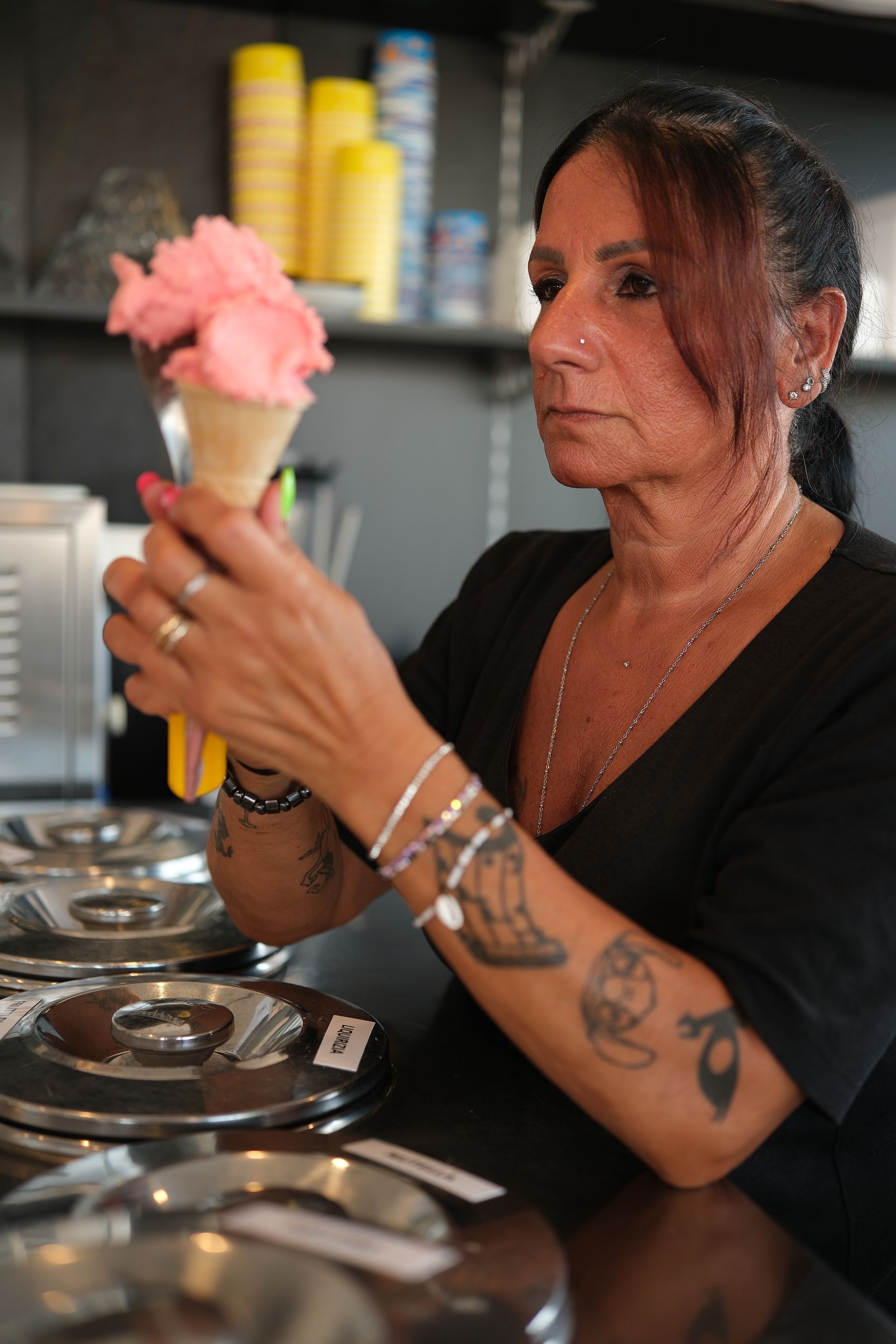 Donna che serve un cono gelato rosa. All'interno di un negozio.