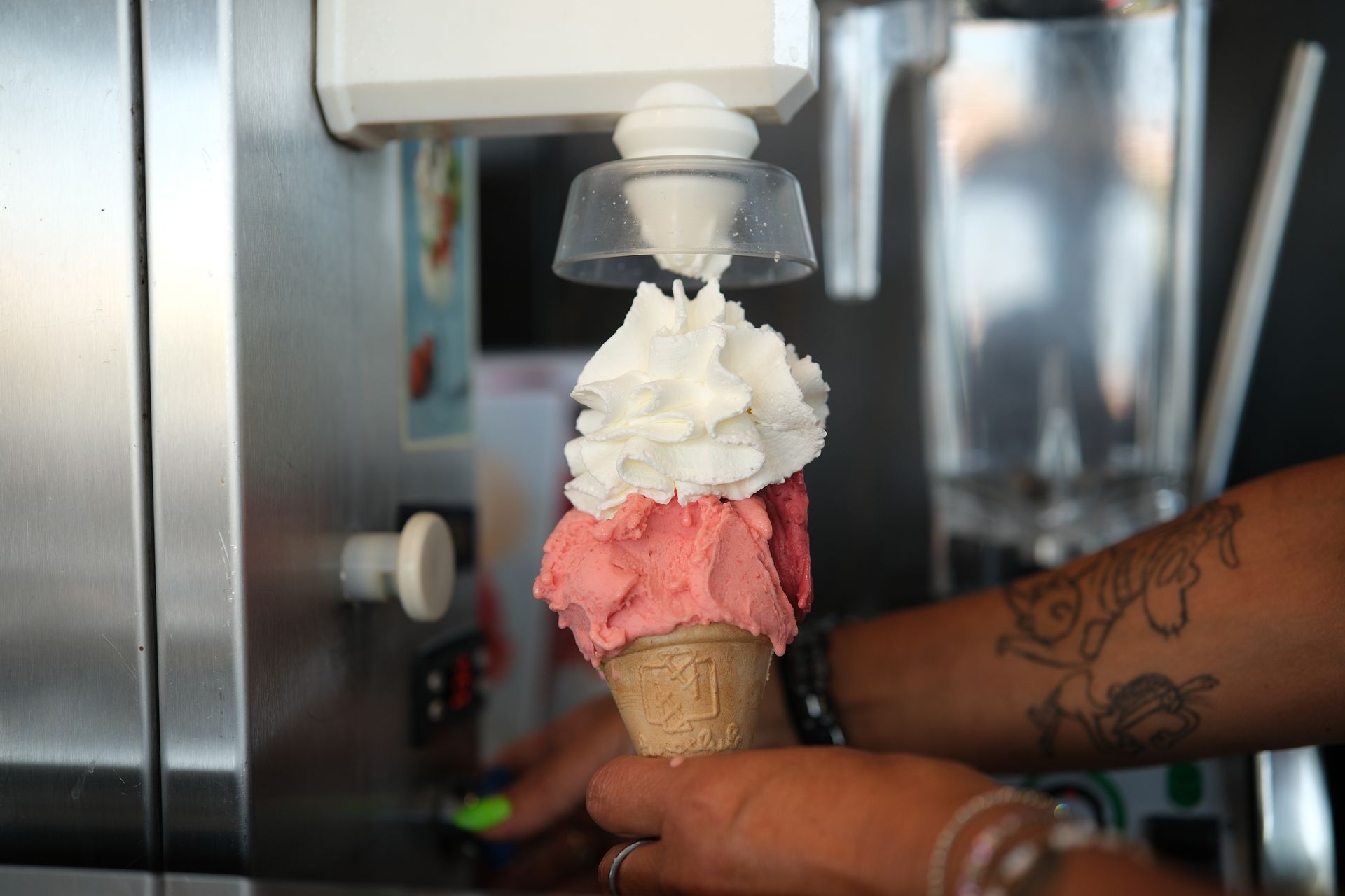 Persona che versa il gelato da una macchina in un cono; strati rosa e bianchi.