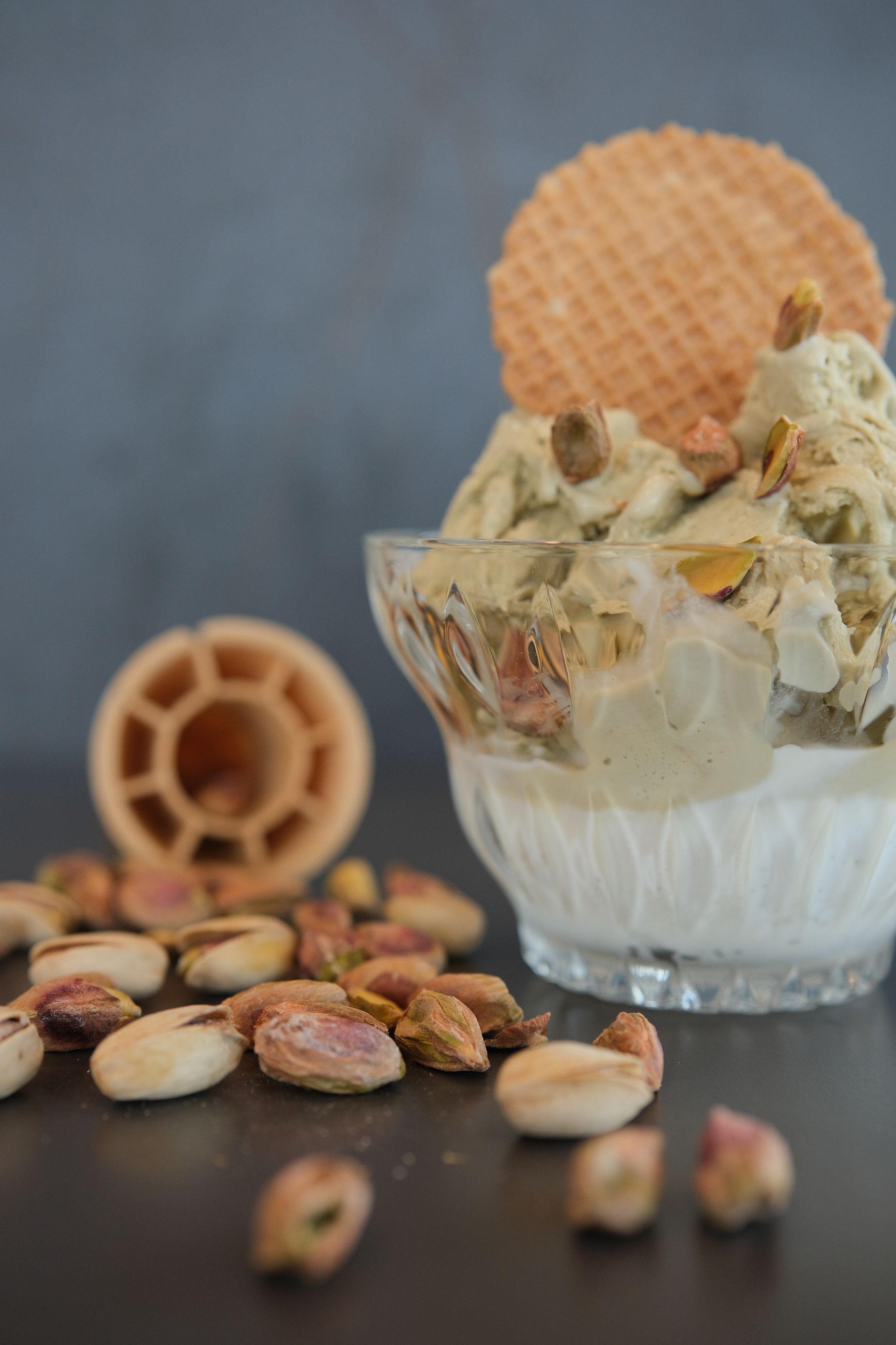 Gelato al pistacchio in una ciotola di vetro, guarnito con una cialda e pistacchi, su una superficie scura.