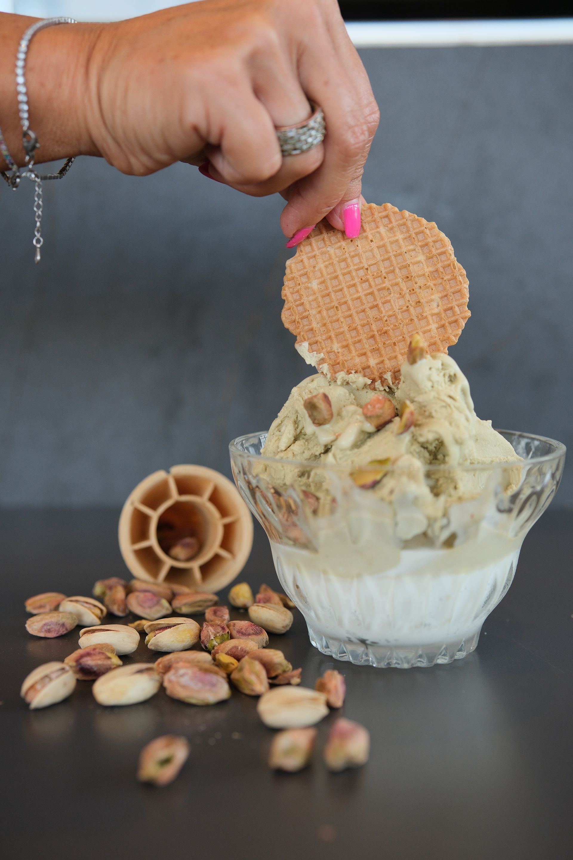 gelato al pistacchio con un biscotto wafer. Pistacchi sparsi, cono di cialda e ciotola di vetro su una superficie scura.