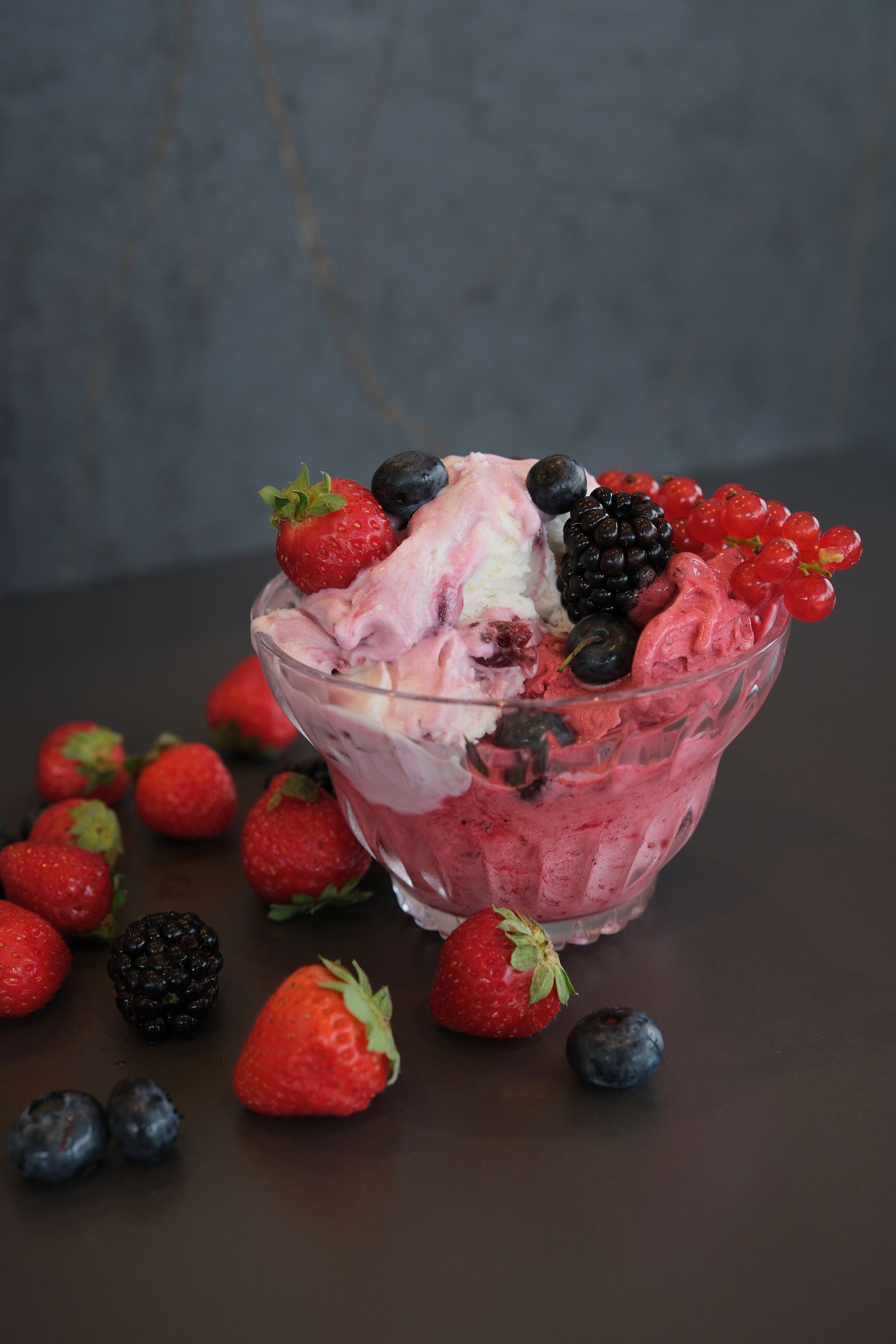 Coppa gelato con frutti di bosco in una ciotola di vetro, circondata da fragole, mirtilli e more sparse.