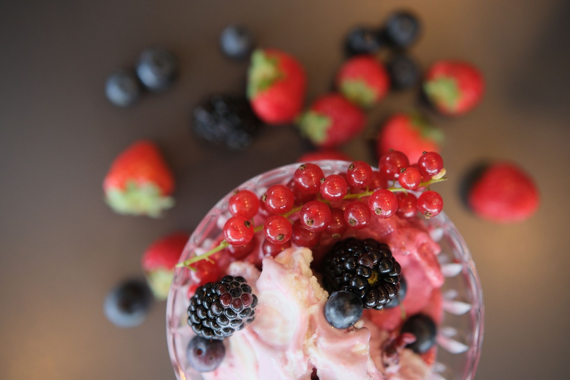 Ciotola di dessert rosa guarnita con ribes rossi, more, mirtilli e fragole su uno sfondo scuro.